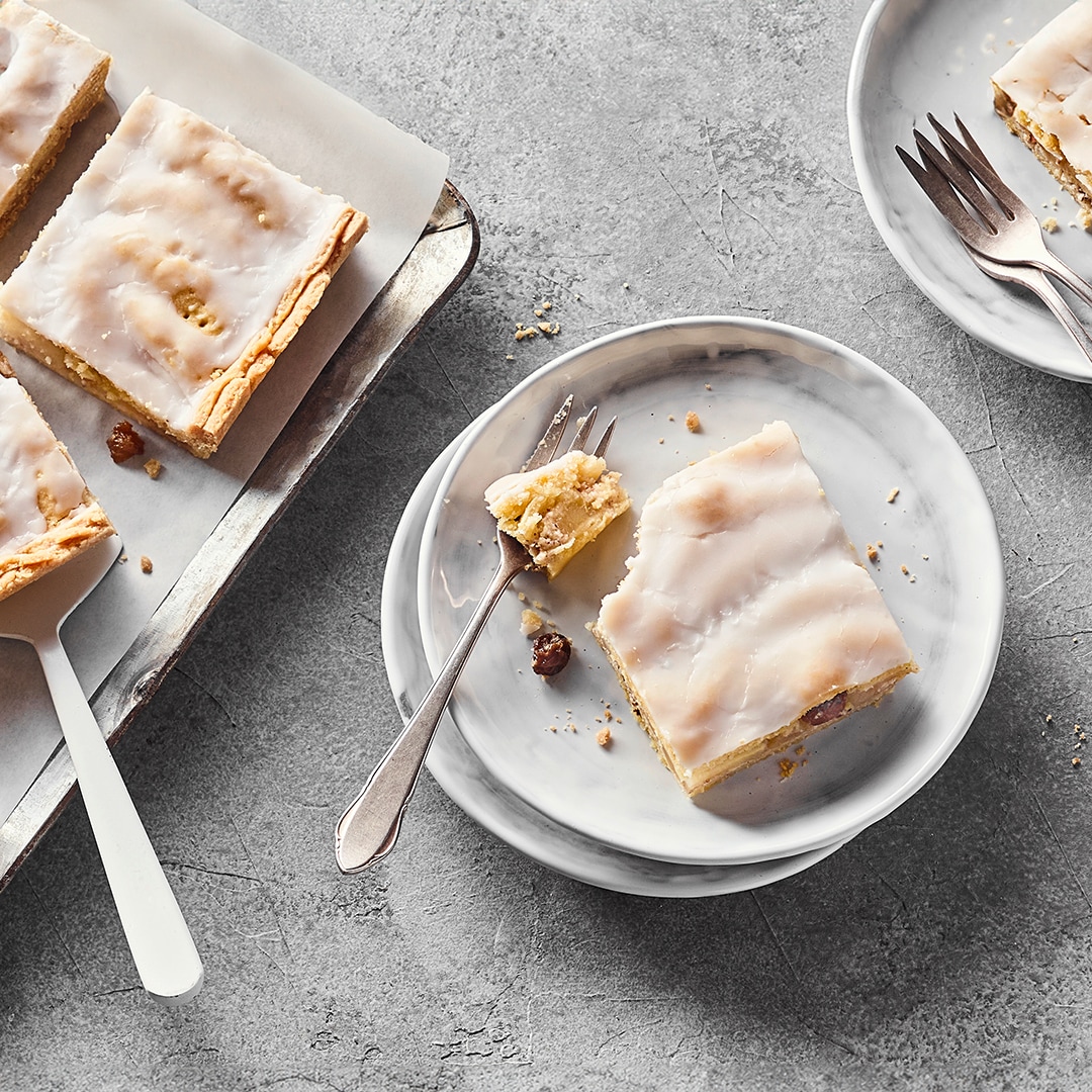 Auf Tellern und einem Backblech Stücke saftiger Apfel-Blechkuchen mit einer Zuckergussglasur