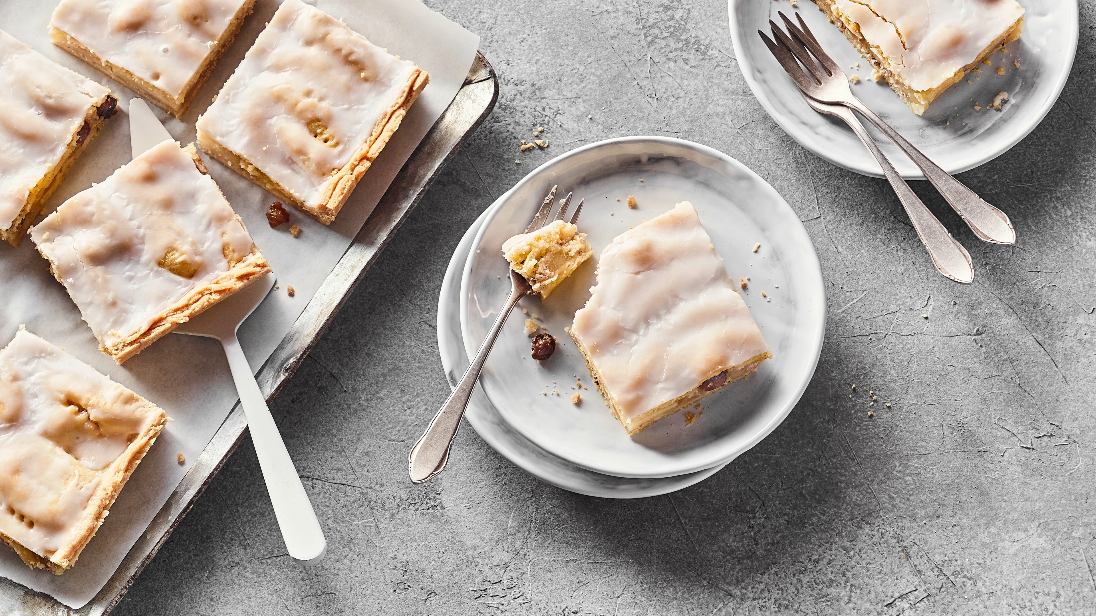Rezept für gedeckten Apfelkuchen vom Blech Auf Tellern und einem Backblech Stücke saftiger Apfel-Blechkuchen mit einer Zuckergussglasur