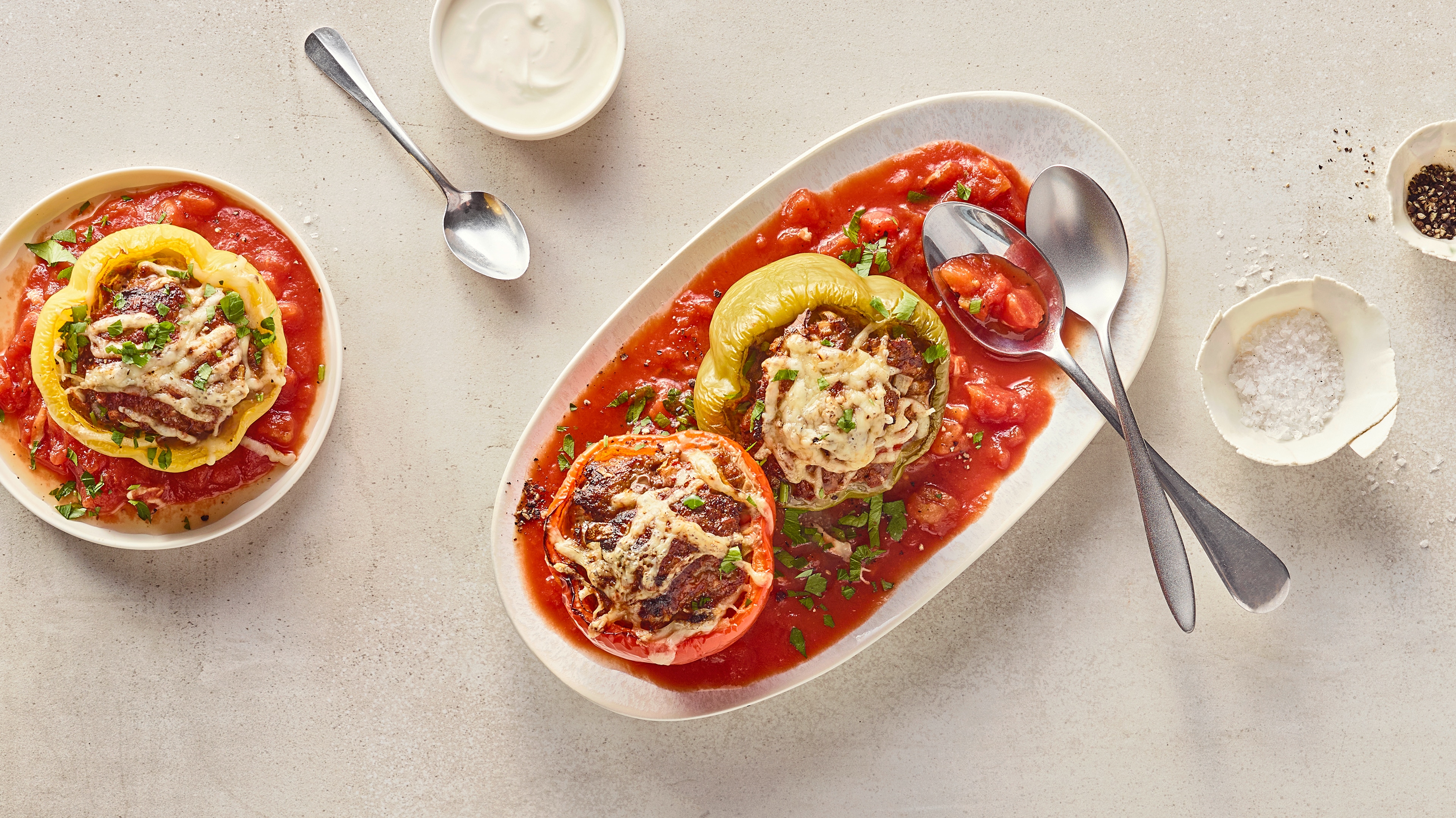 Rezept für gefüllte Paprika aus der Heißluftfritteuse Eine rote und eine grüne Paprika, gefüllt mit Fleisch, getoppt mit Käse in einer tomatigen Soße, auf einer ovalen Schale