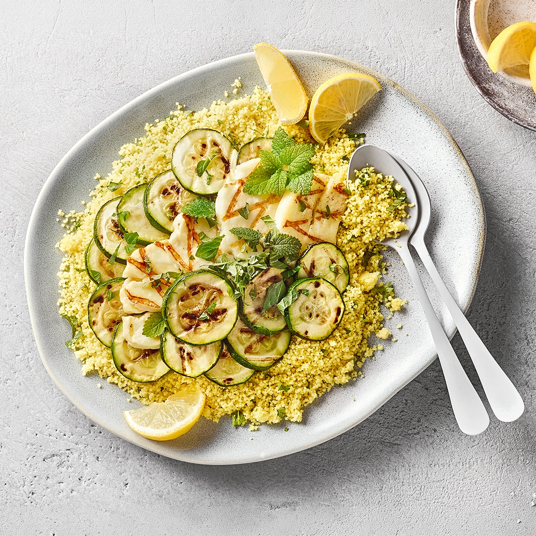 Großer Teller Couscous mit gegrillter Zucchini und Halloumi, garniert mit Minze und Zitronenspalten.