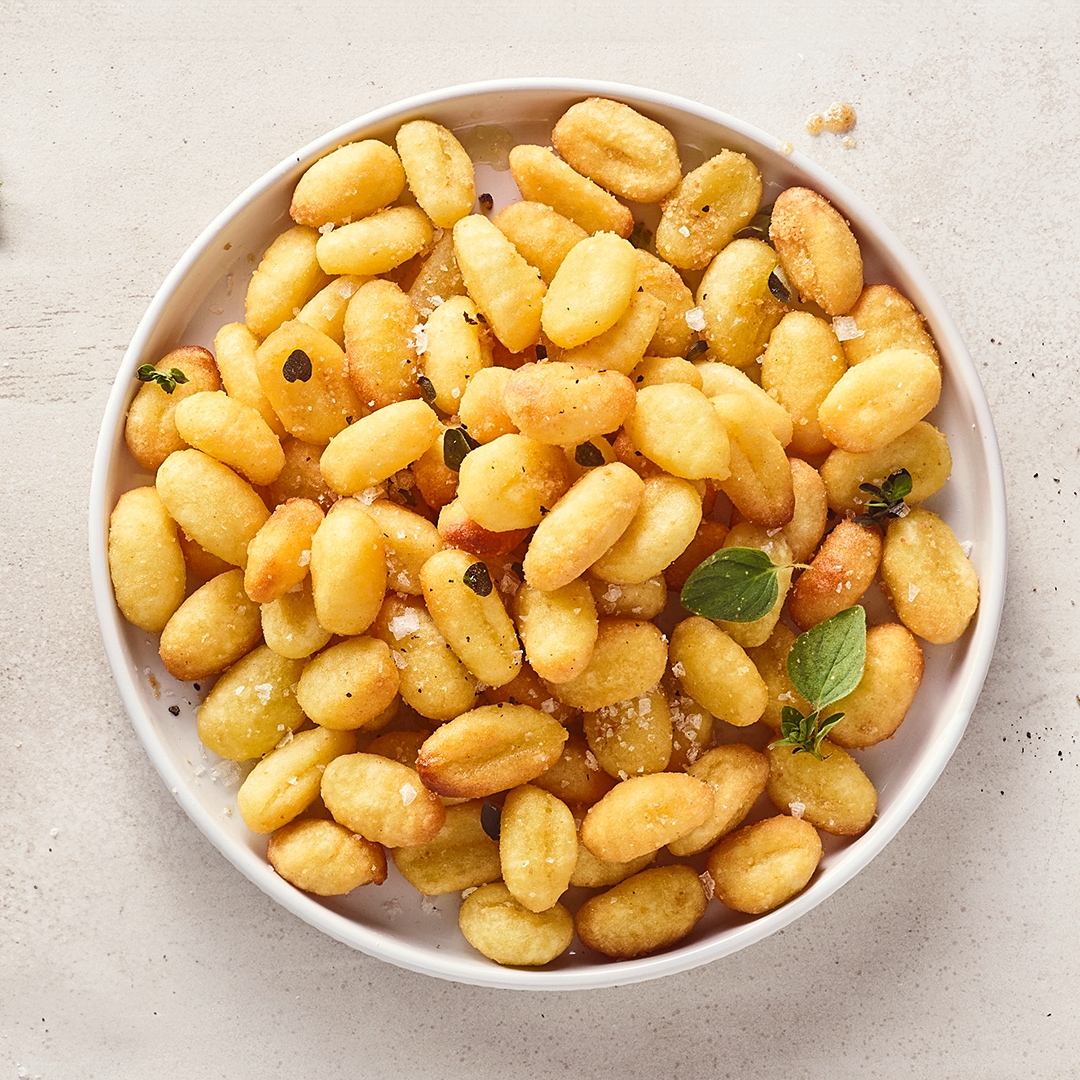 Ein runder Teller mit gelbgoldenen, knusprigen Gnocchi, getoppt mit frischem Thymian und flockiges Salz
