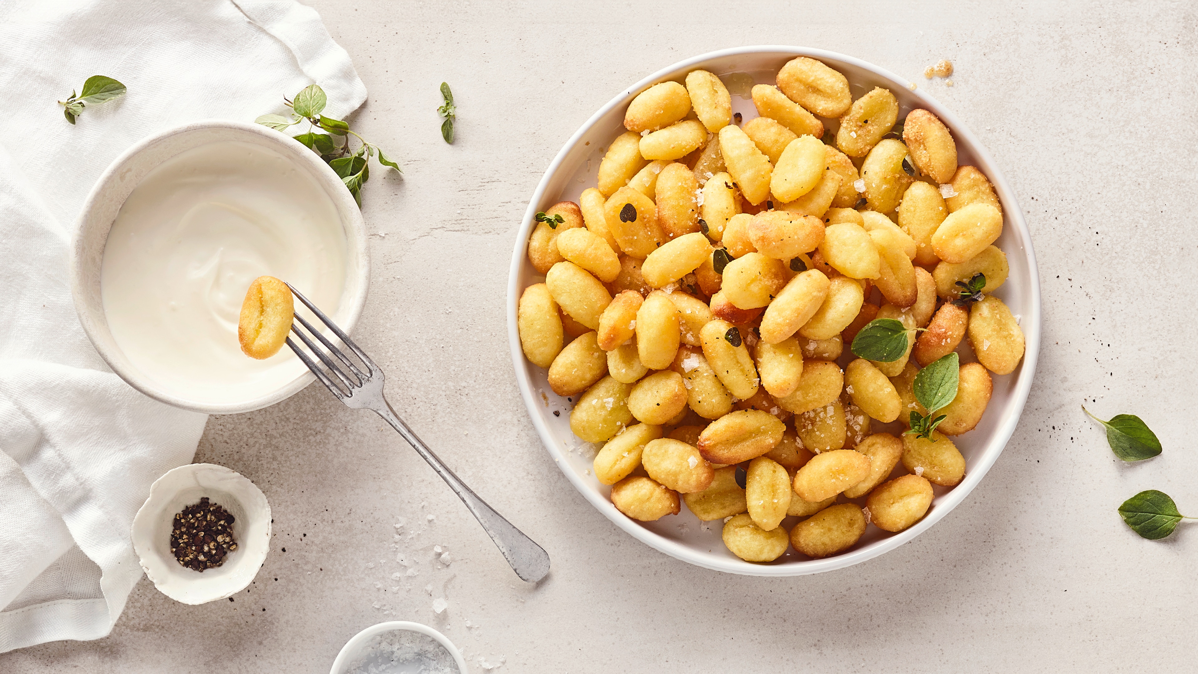 Rezept für Gnocchi aus dem Airfryer Ein runder Teller mit gelbgoldenen, knusprigen Gnocchi, getoppt mit frischem Thymian und flockiges Salz