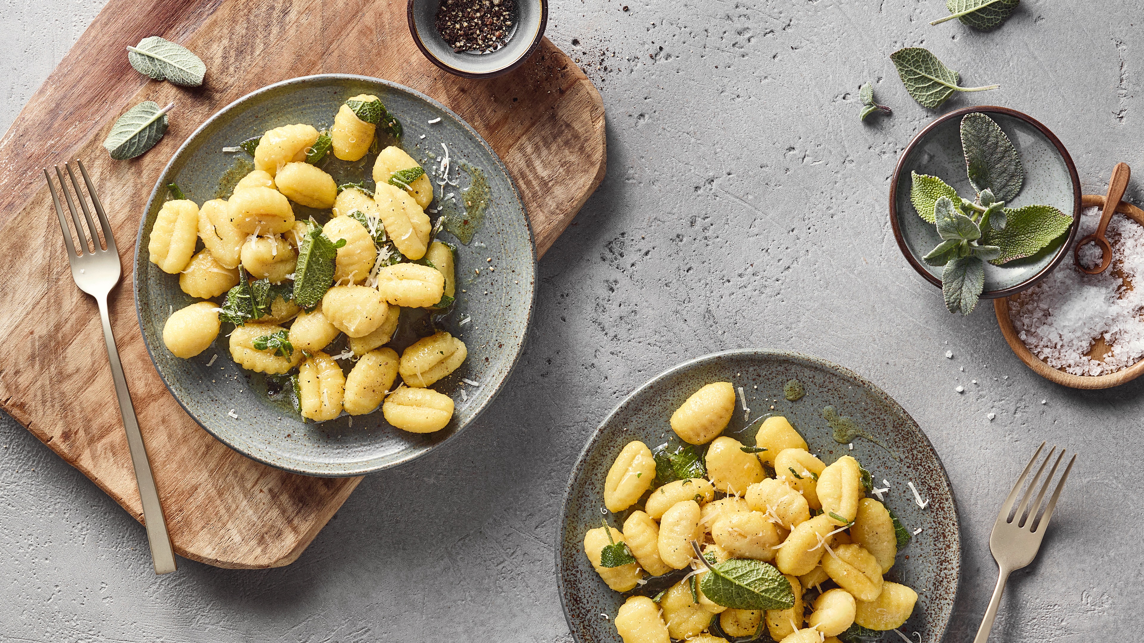 Ein Teller mit Gnocchi, darauf grüne Blätter und etwas hellem geriebenem Belag, umgeben von klarer Soße.
