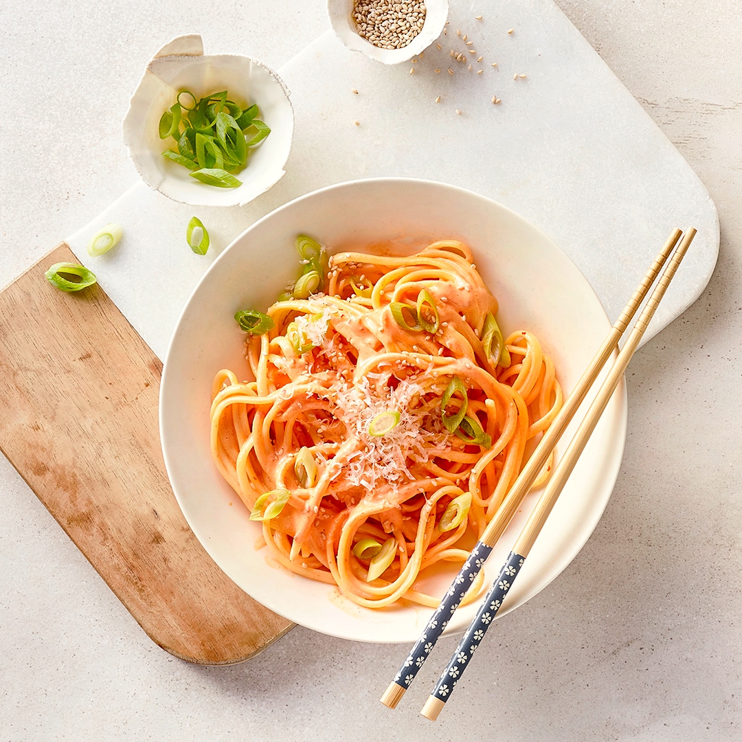 Ein Teller mit Spaghetti in heller, roter Soße, garniert mit geschnittenen Frühlingszwiebeln, Sesam und geriebenem Käse