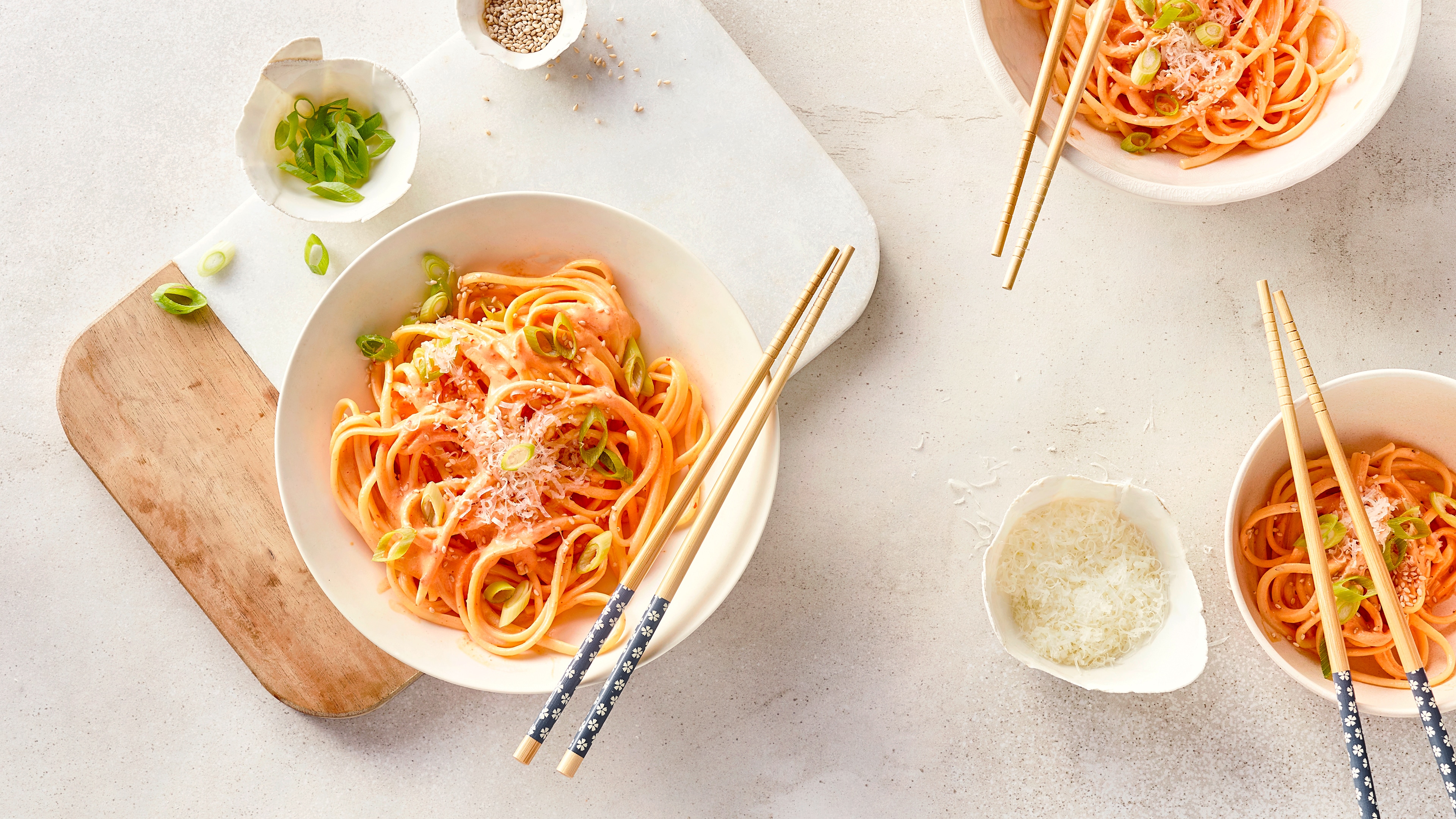 Ein Teller mit Spaghetti in heller, roter Soße, garniert mit geschnittenen Frühlingszwiebeln, Sesam und geriebenem Käse