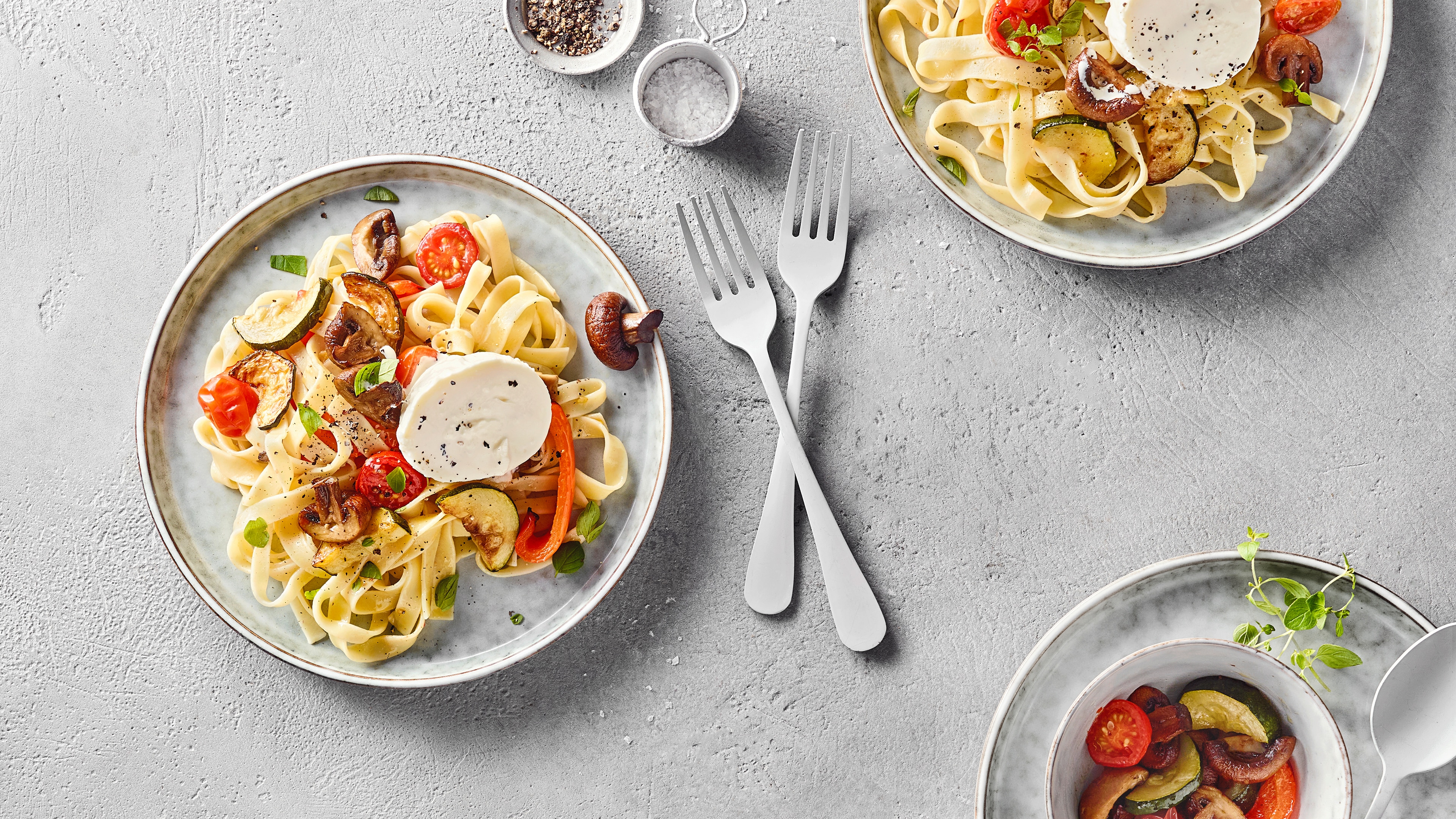 Drei Teller Bandnudeln mit gegrilltem Gemüse und Burrata, dekoriert mit frischen Kräutern.