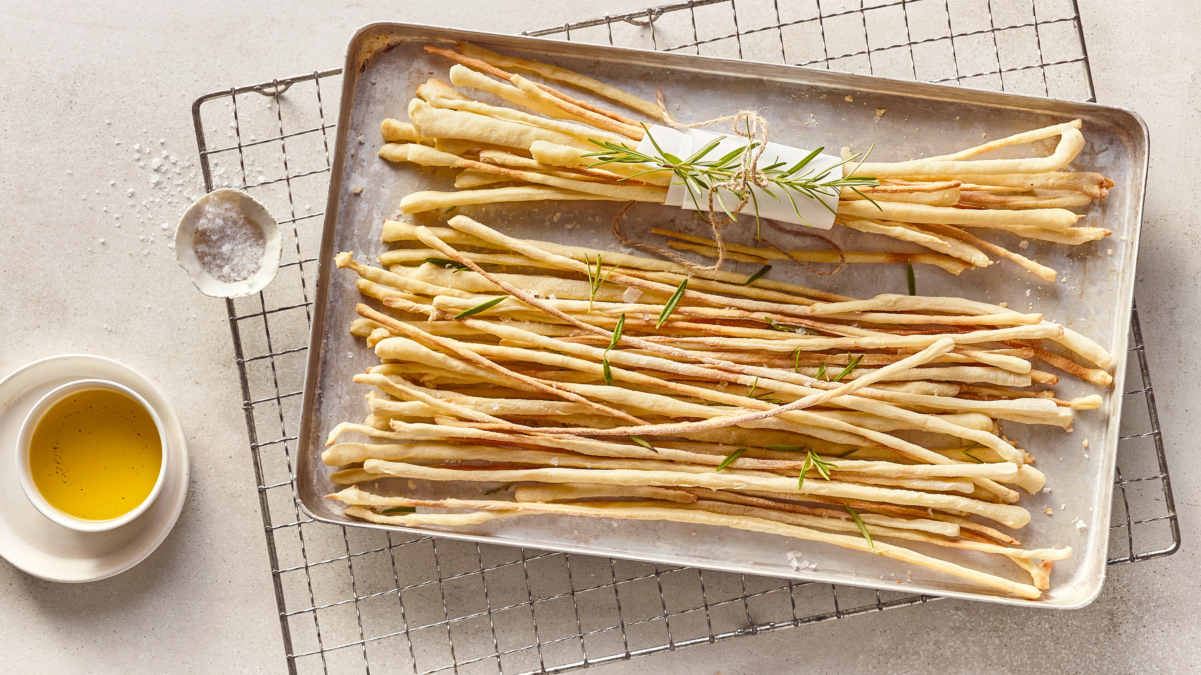 Rezept für italienische Grissini Ein metallisches Backblech mit sehr dünnen, sehr langen Brotstangen, getoppt mit frischem Rosmarin