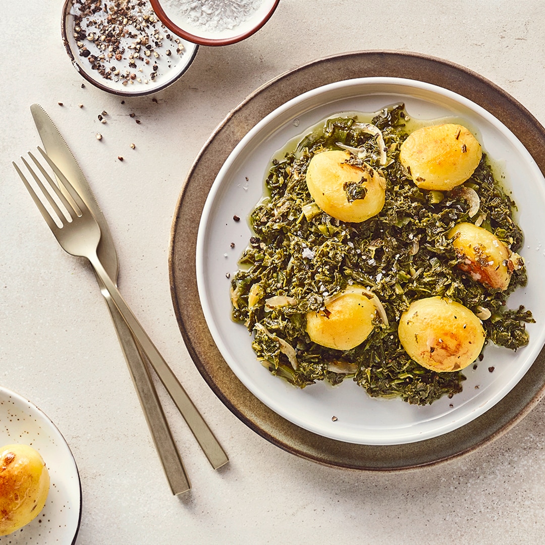 Teller mit Grünkohl und kleinen Kartoffeln, daneben Schälchen mit Salz und Pfeffer