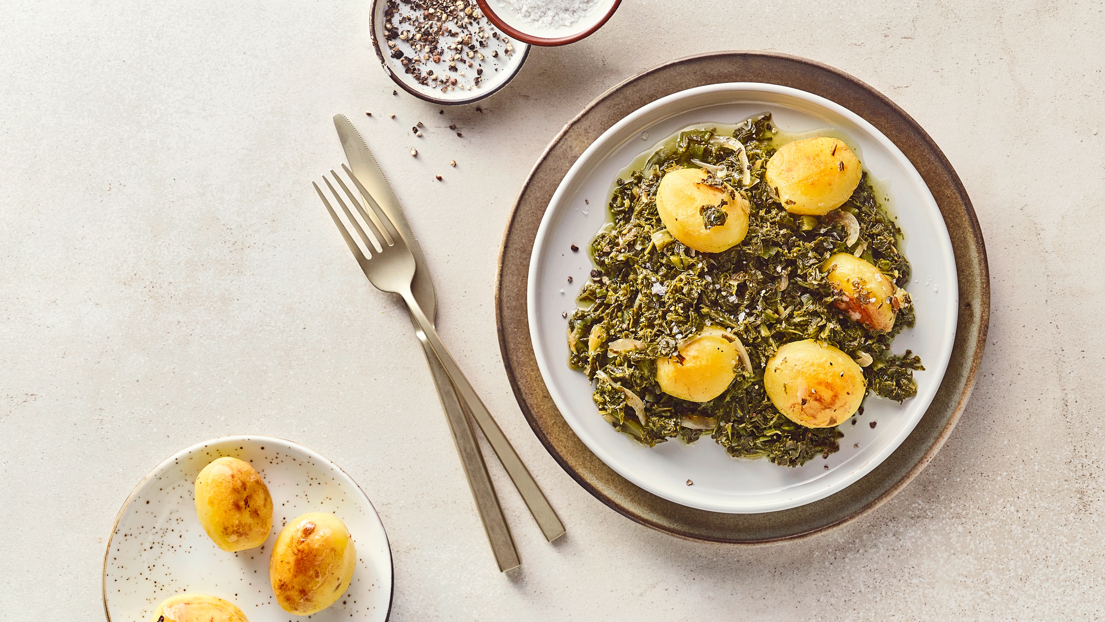Teller mit Grünkohl und kleinen Kartoffeln, daneben Schälchen mit Salz und Pfeffer