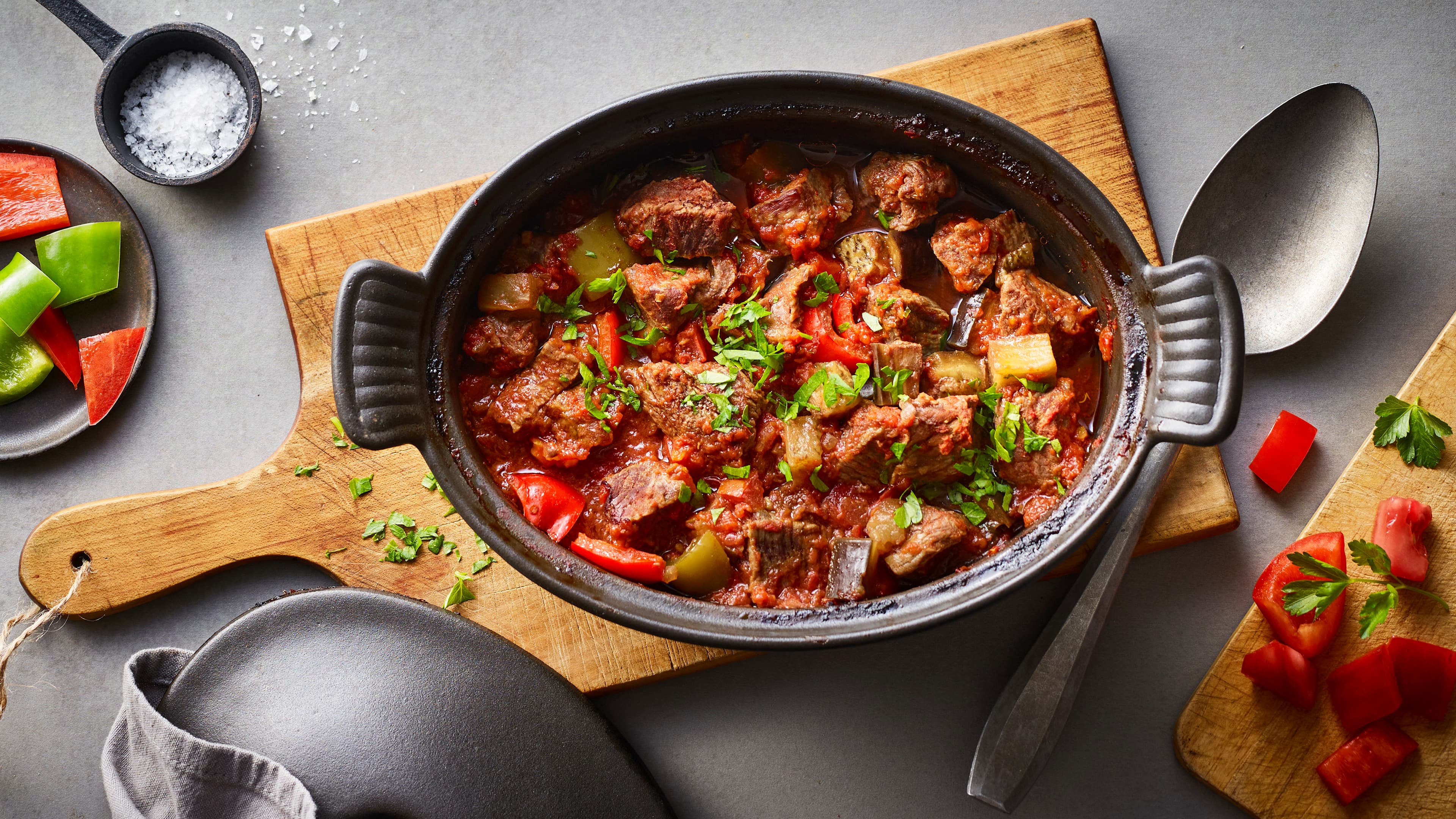 Rezept für türkisches Güvec Ein gusseisener Topf mit Fleisch und Paprika in rotbrauner Soße, getoppt mit frischer, gehackter Petersilie