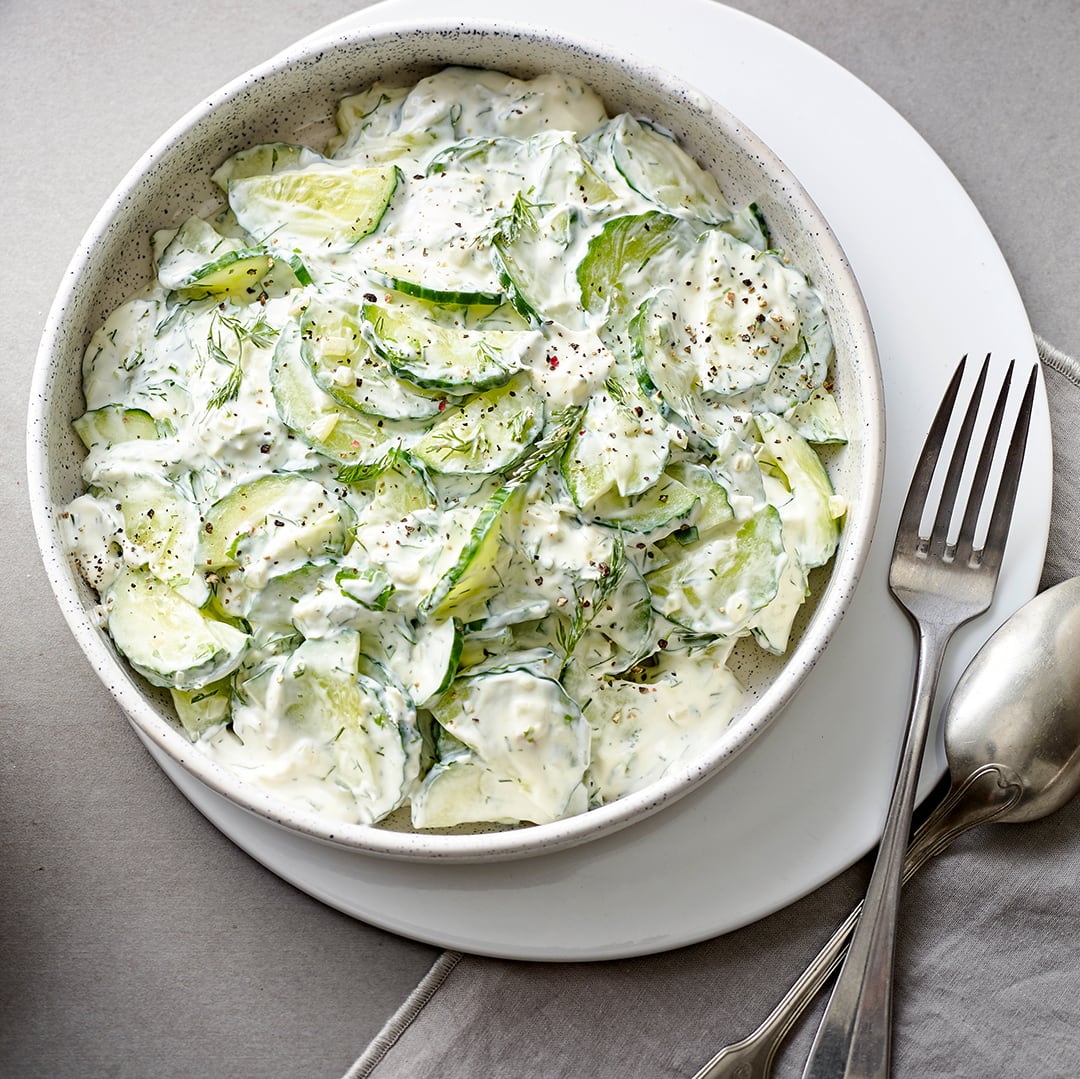 Eine Schüssel mit Gurkenscheiben in einer weißen, cremigen Soße, dekoriert mit Dill und gemahlenem Pfeffer