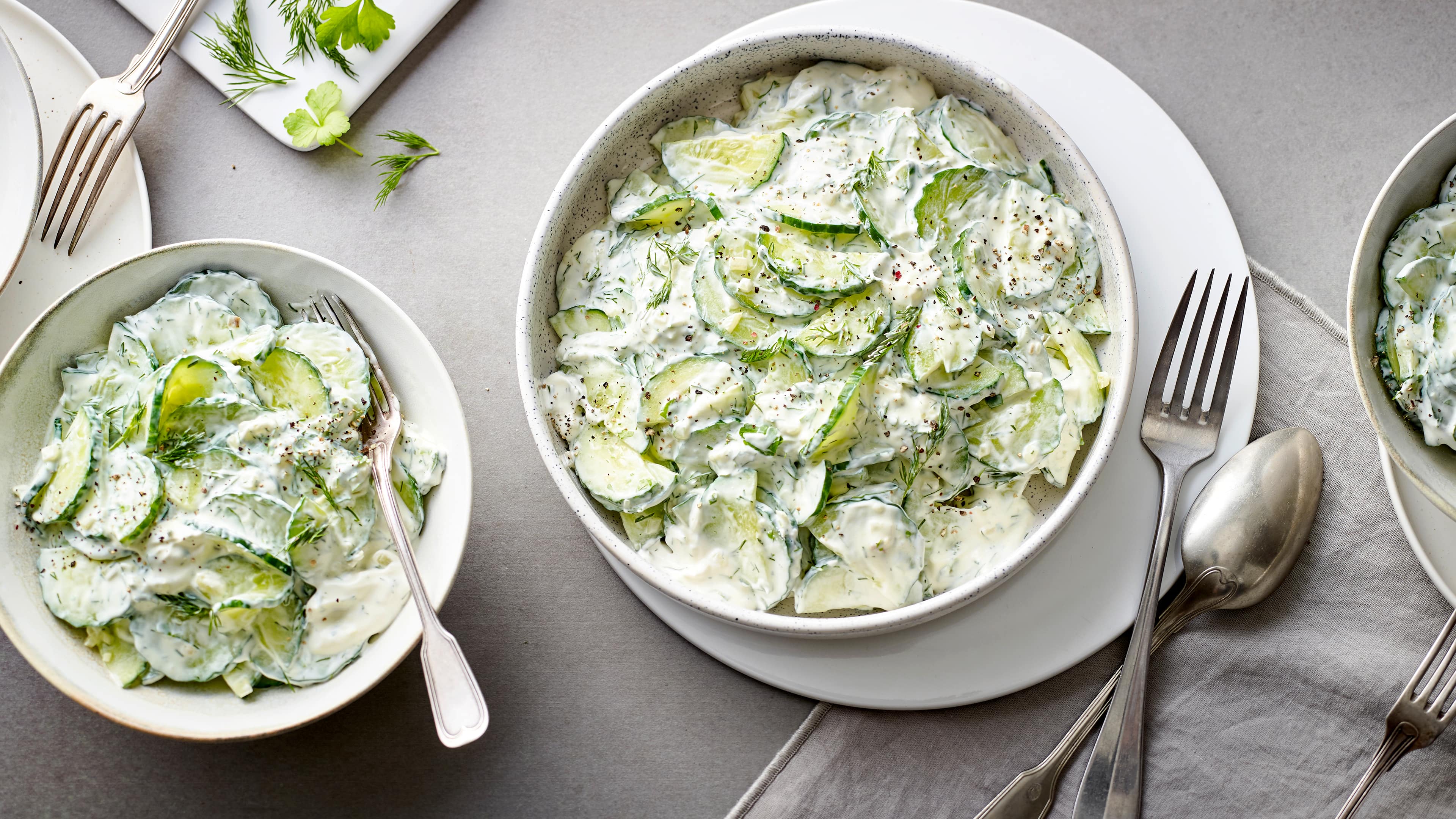 Zwei Schüsseln mit Gurkenscheiben in einer weißen, cremigen Soße, dekoriert mit Dill und gemahlenem Pfeffer