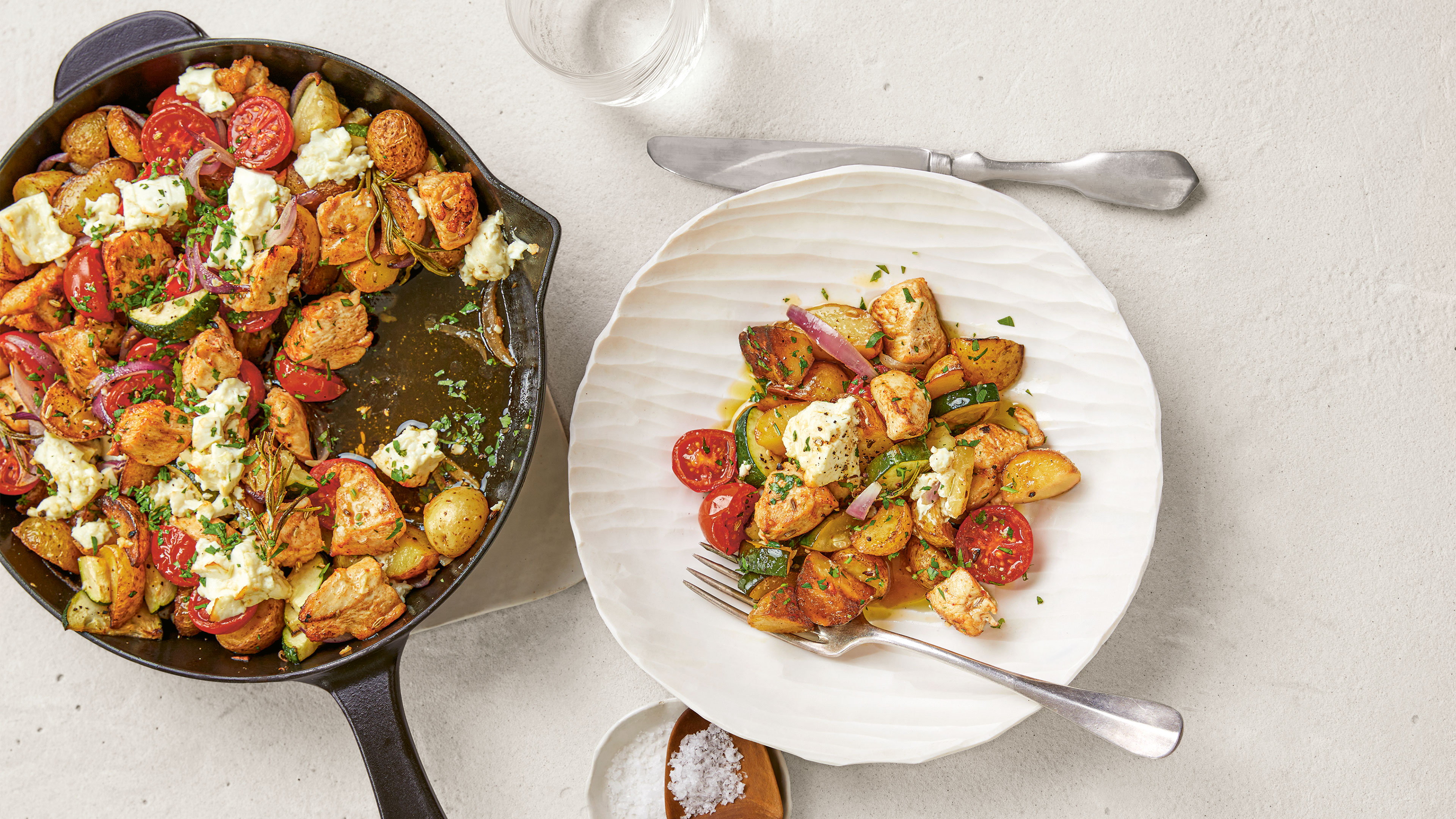 Pfanne mit Kartoffelstücken, Hähnchenstücken, Tomaten und Zucchinischeiben. Daneben ein Teller mit dem Pfannengericht
