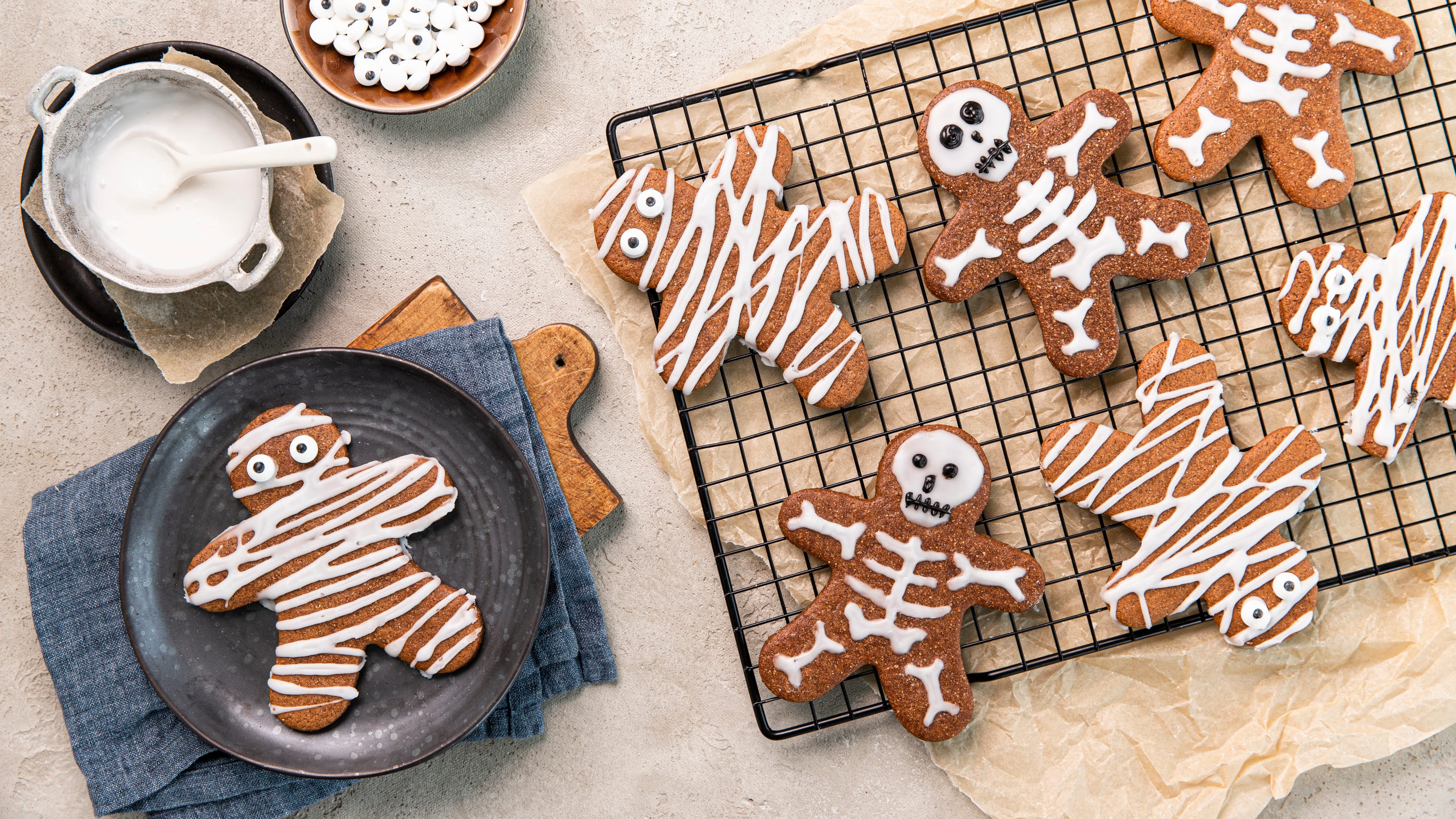 Rezept für Halloween-Lebkuchen-Kekse Ein Abkühlgitter mit Lebkuchen-Keks-Männchen, mit weißem und schwarzen Zuckerguss als Mumien und Skelette dekoriert