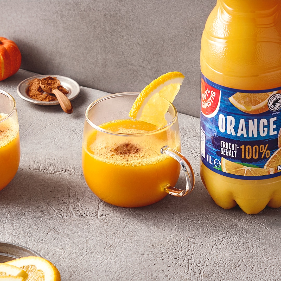 Glas mit heißem Orangensaft und Zitronenscheibe auf einem Tisch, daneben eine Flasche GUT&GÜNSTIG Orangensaft.