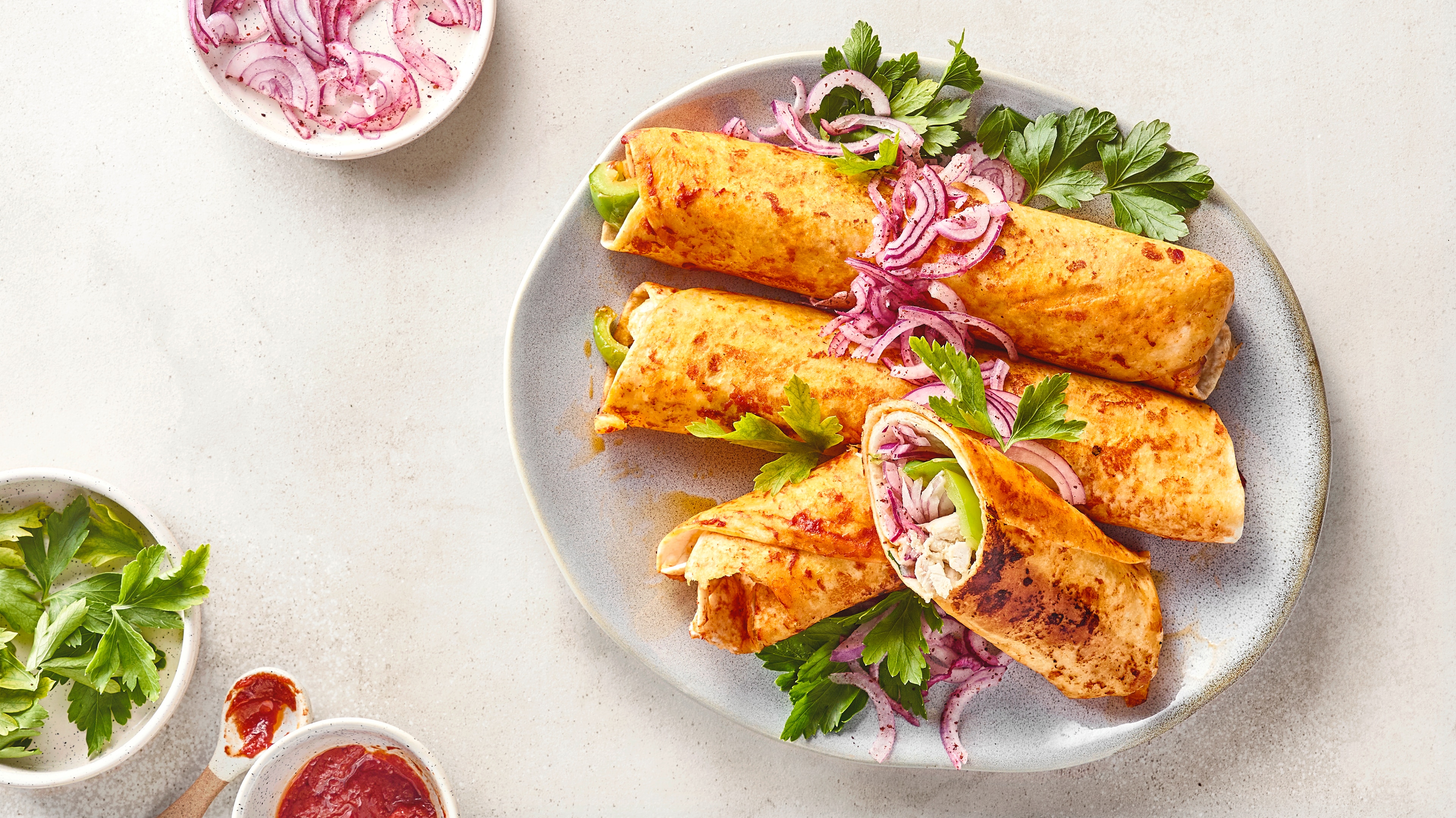 Goldbraun gebratene Wraps mit Füllung, roten Zwiebeln und Petersilie auf einem Teller, serviert mit Salsa.