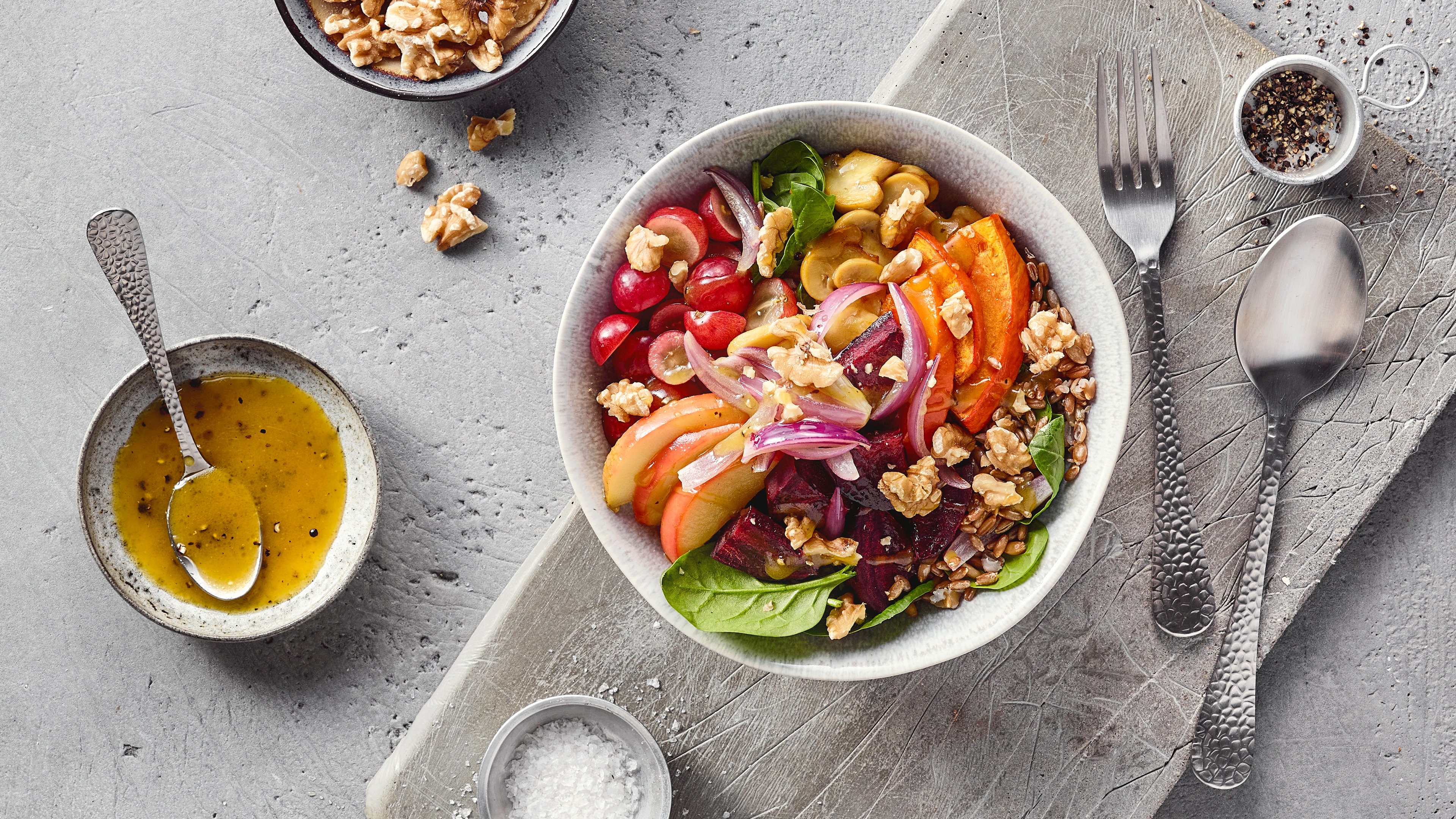 Eine Schüssel mit roten Trauben, Apfelscheiben, Kürbisstücken, roten Zwiebeln, grünen Blättern und Walnüssen.