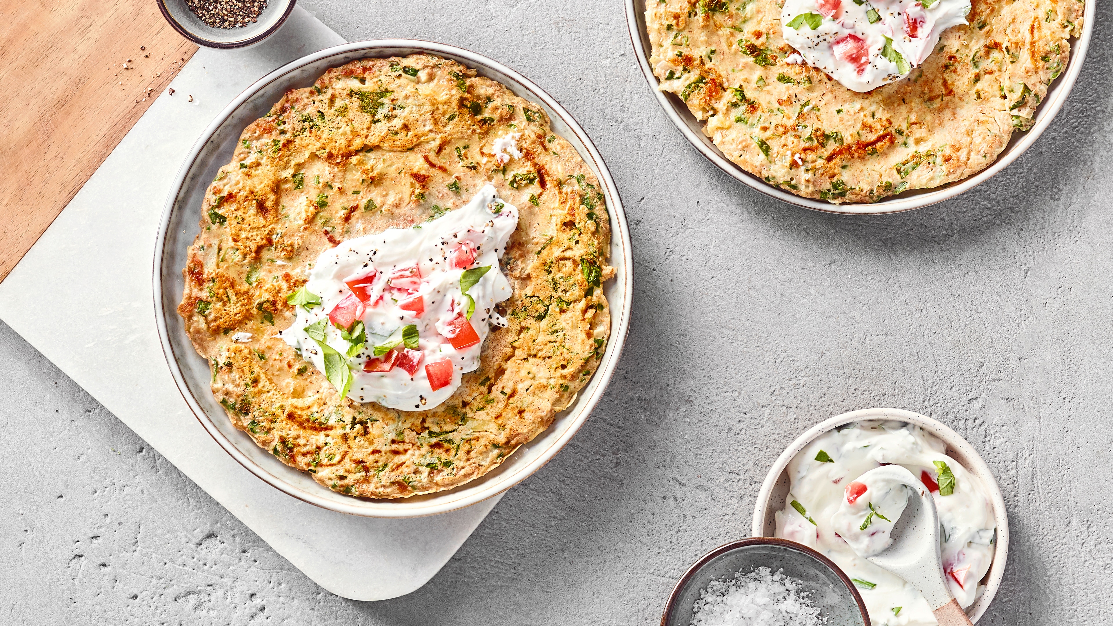 Ein Teller mit gelbgoldenen Pfannkuchen mit Quark-Joghurt-Dip, Tomaten und frischen Kräutern