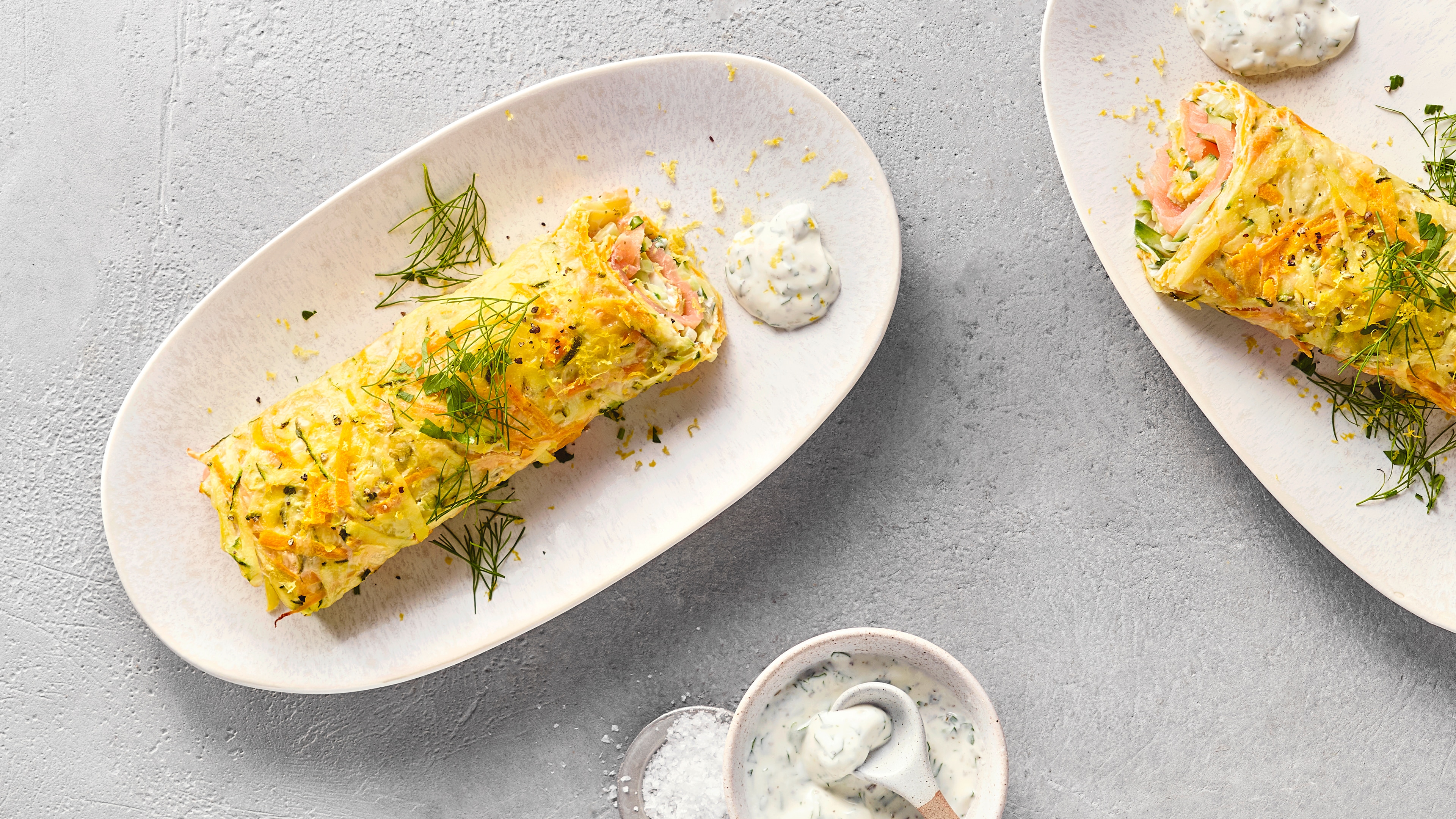 Gemüserollen mit Lachs und Kräuterfrischkäse, garniert mit Dill, daneben eine Schale Kräuterfrischkäse.