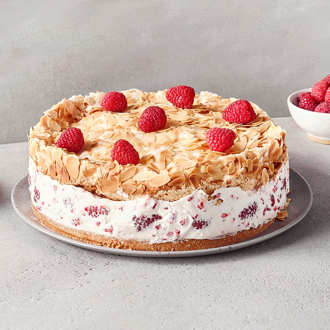 Ein Teller mit einem runden Kuchen, weißer Creme mit Himbeeren, einer Schicht aus Mandelblättchen & roten Himbeeren obenauf.