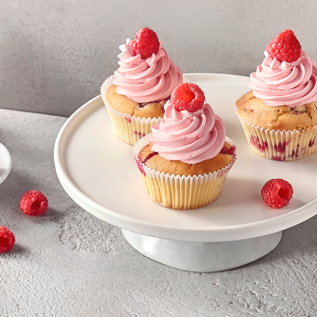 Eine Etagere mit Cupcakes aus hellem Teig, gefüllt mit Himbeeren, getoppt mit Himbeercreme.