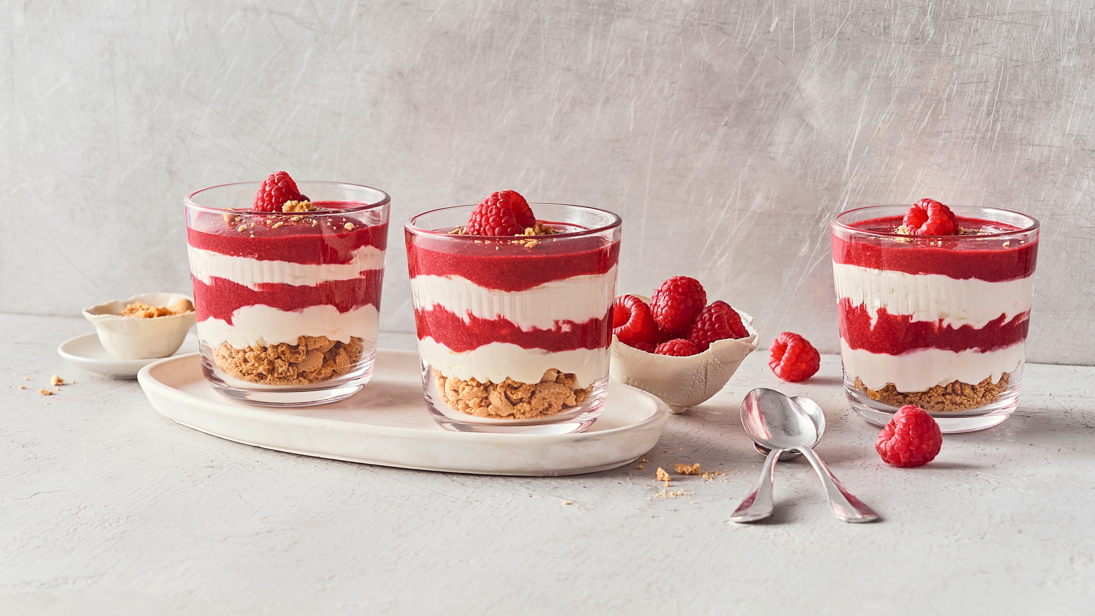 Rezept für Himbeer Mascarpone Dessert Dessertgläser, befüllt mit Keksstückchen, darüber geschichtet helle und himbeerfarbige Creme, garniert mit frischen Himbeeren
