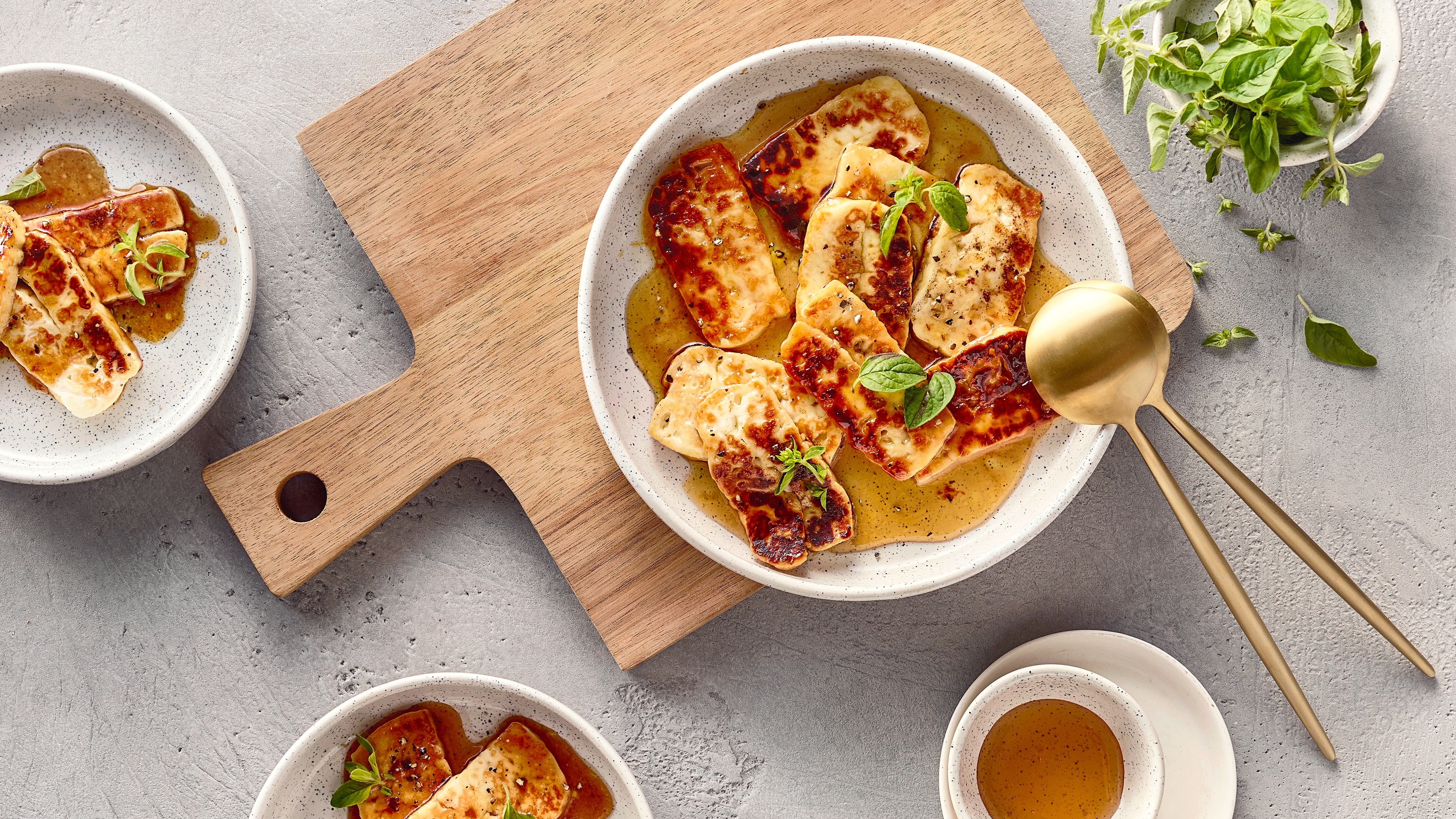 Rezept für Honey glazed Halloumi Ein Teller mit goldbraun gebratenem Halloumi, in einer hellen Flüssigkeit, garniert mit frischem Basilikum