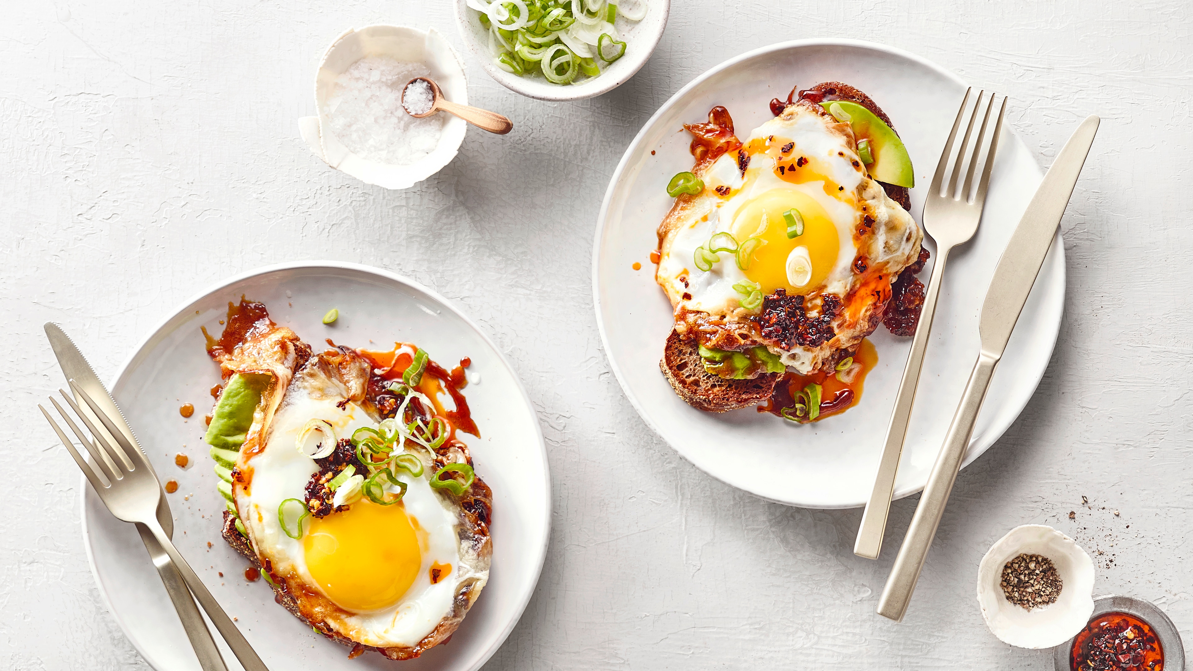 Zwei Teller mit jeweils einem Spiegelei, gewürzt mit Chili-Öl und Frühlingszwiebeln.