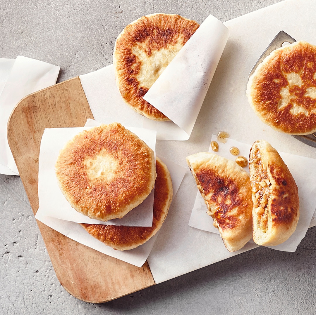 Ein Holzbrett mit mehreren runden, goldbraun gebackenen Teigtaschen, gefüllt mit einer süßen, körnigen Masse