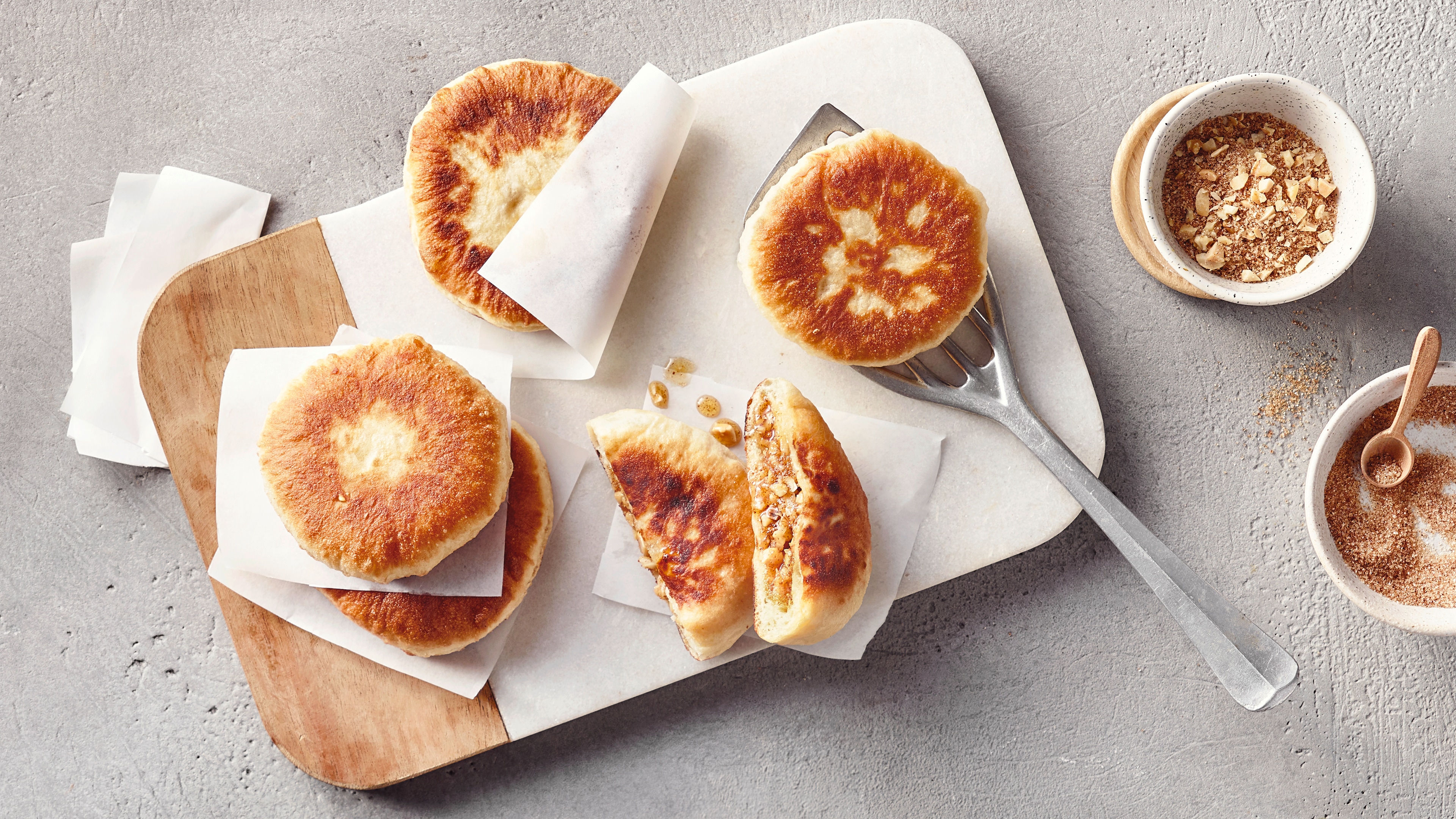 Ein Holzbrett mit mehreren runden, goldbraun gebackenen Teigtaschen, gefüllt mit einer süßen, körnigen Masse