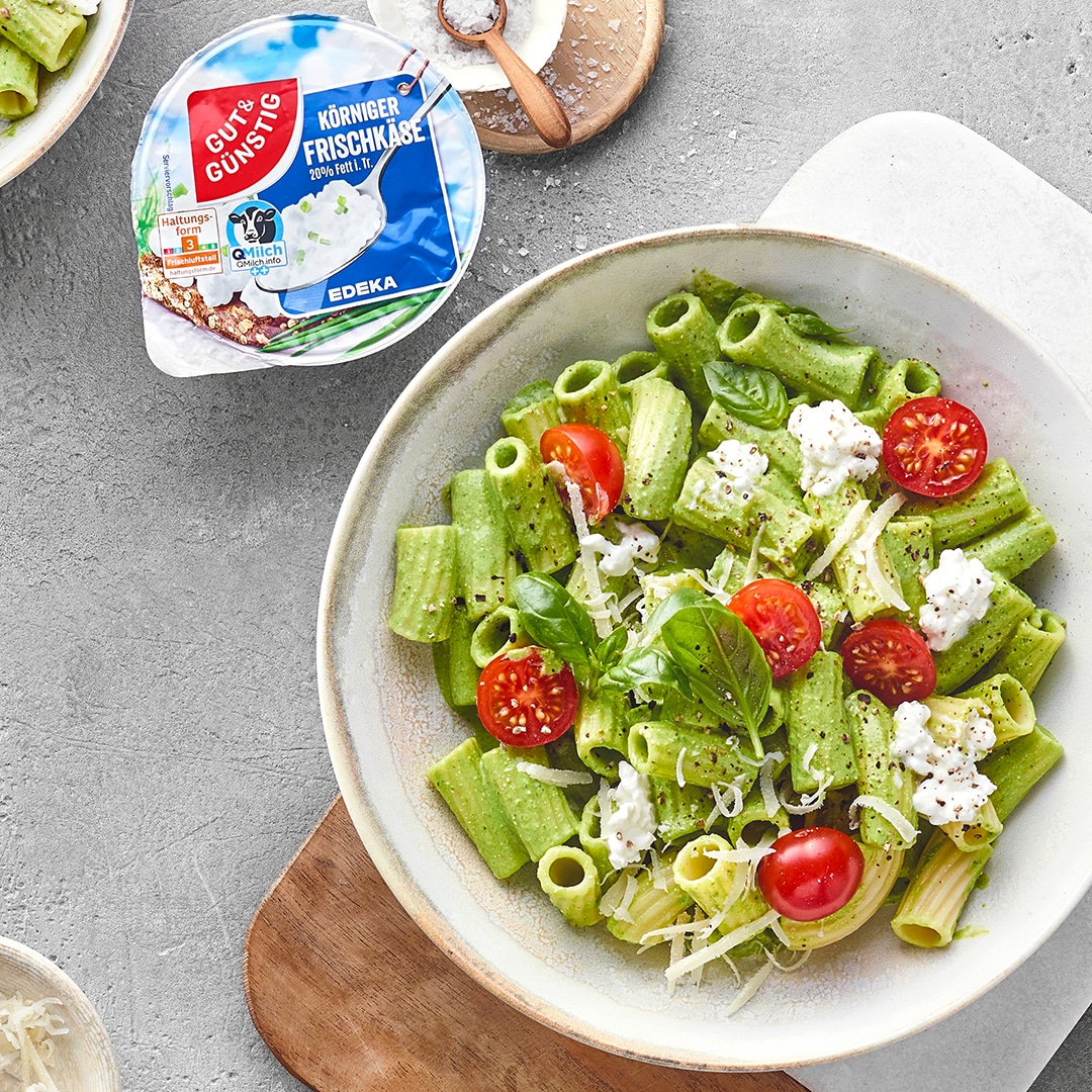 Teller mit Rigatoni Nudeln mit grüner Soße, Hüttenkäse und Tomaten. Daneben das Produkt Gut&Günstig Körniger Frischkäse