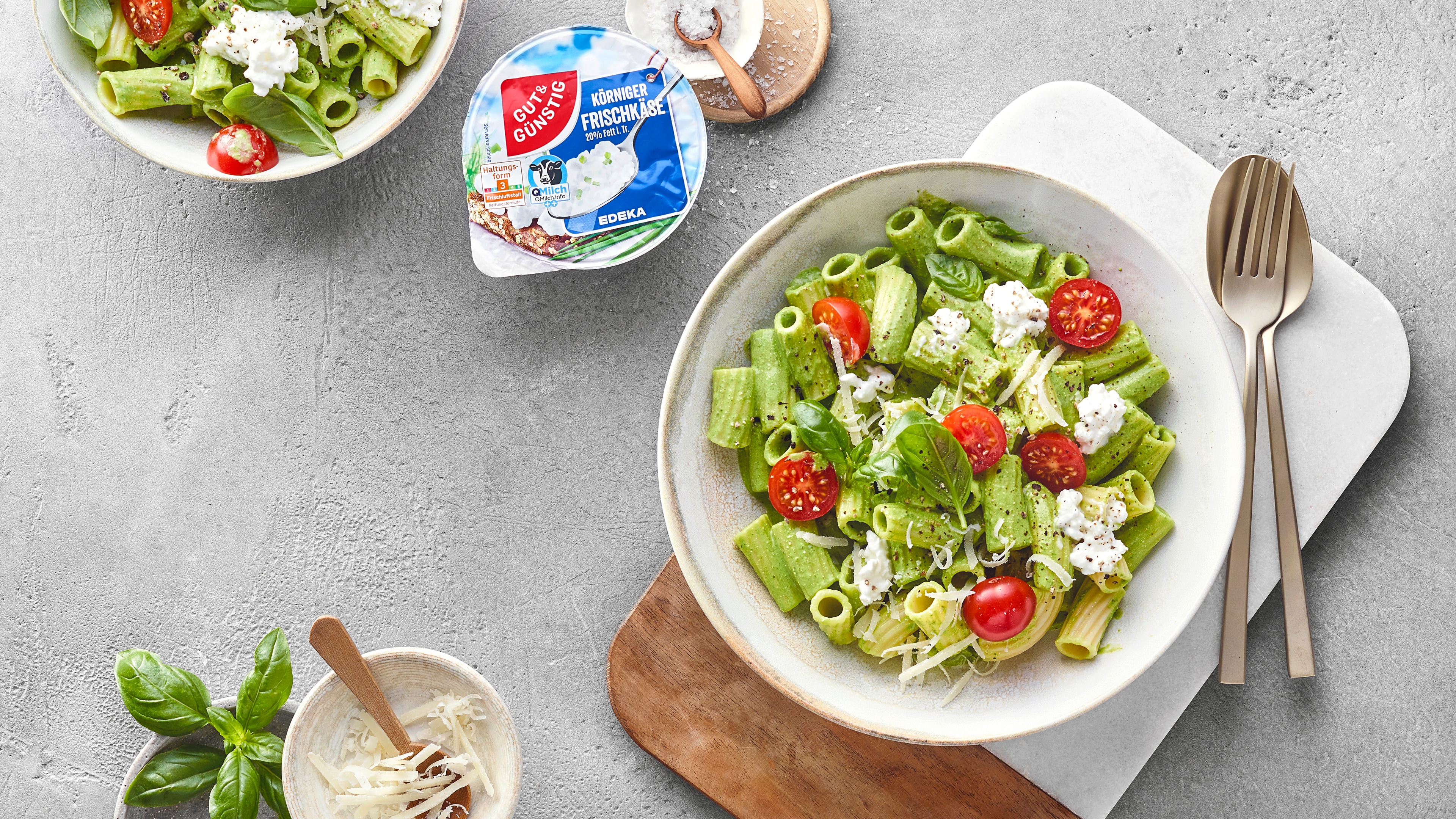 Teller mit Rigatoni Nudeln mit grüner Soße, Hüttenkäse und Tomaten. Daneben das Produkt Gut&Günstig Körniger Frischkäse