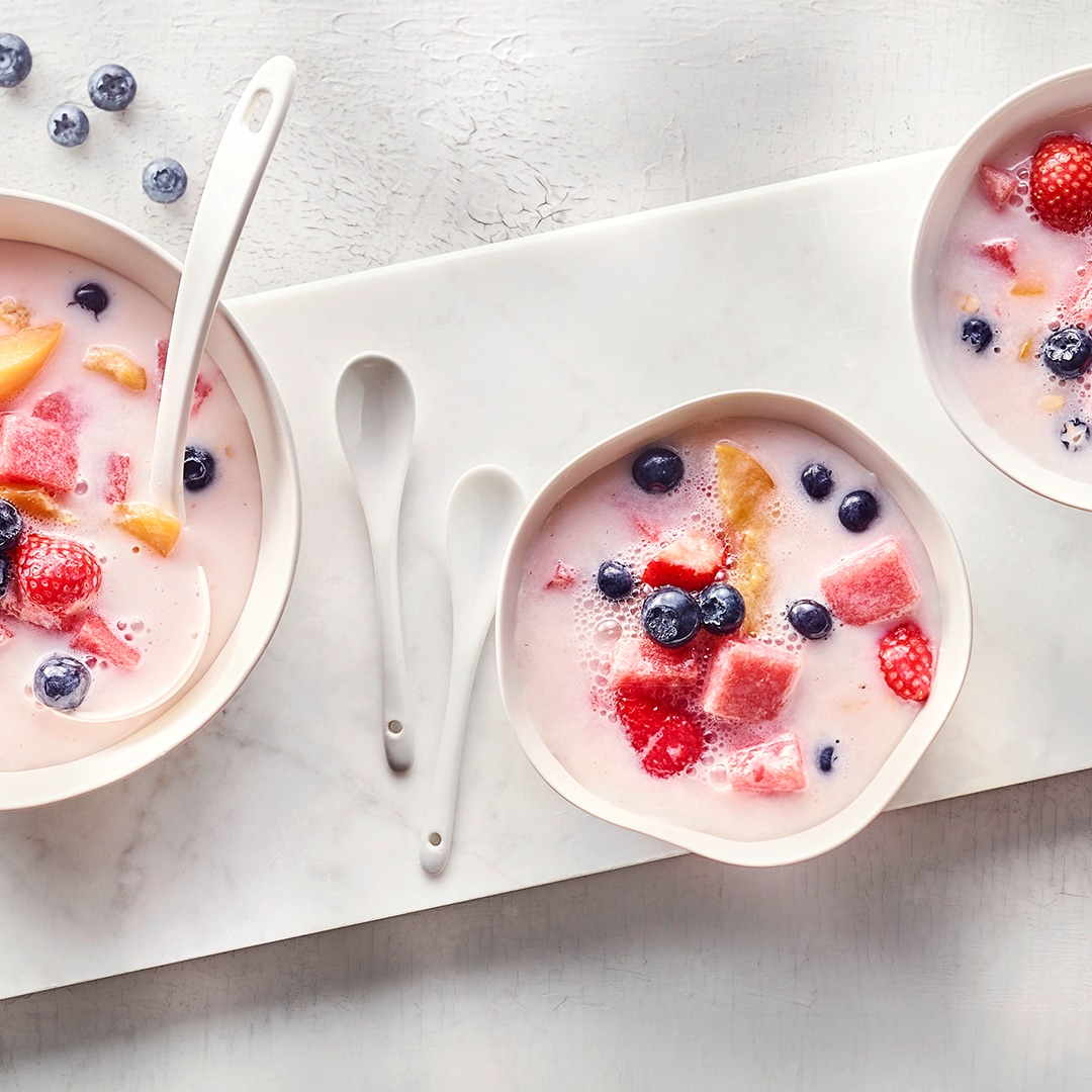 Kleine Schälchen, gefüllt mit hellrosa, milchiger Fruchtpunsch mit frischen Erdbeeren, Blaubeeren, Pfirsich und Wassermelone.