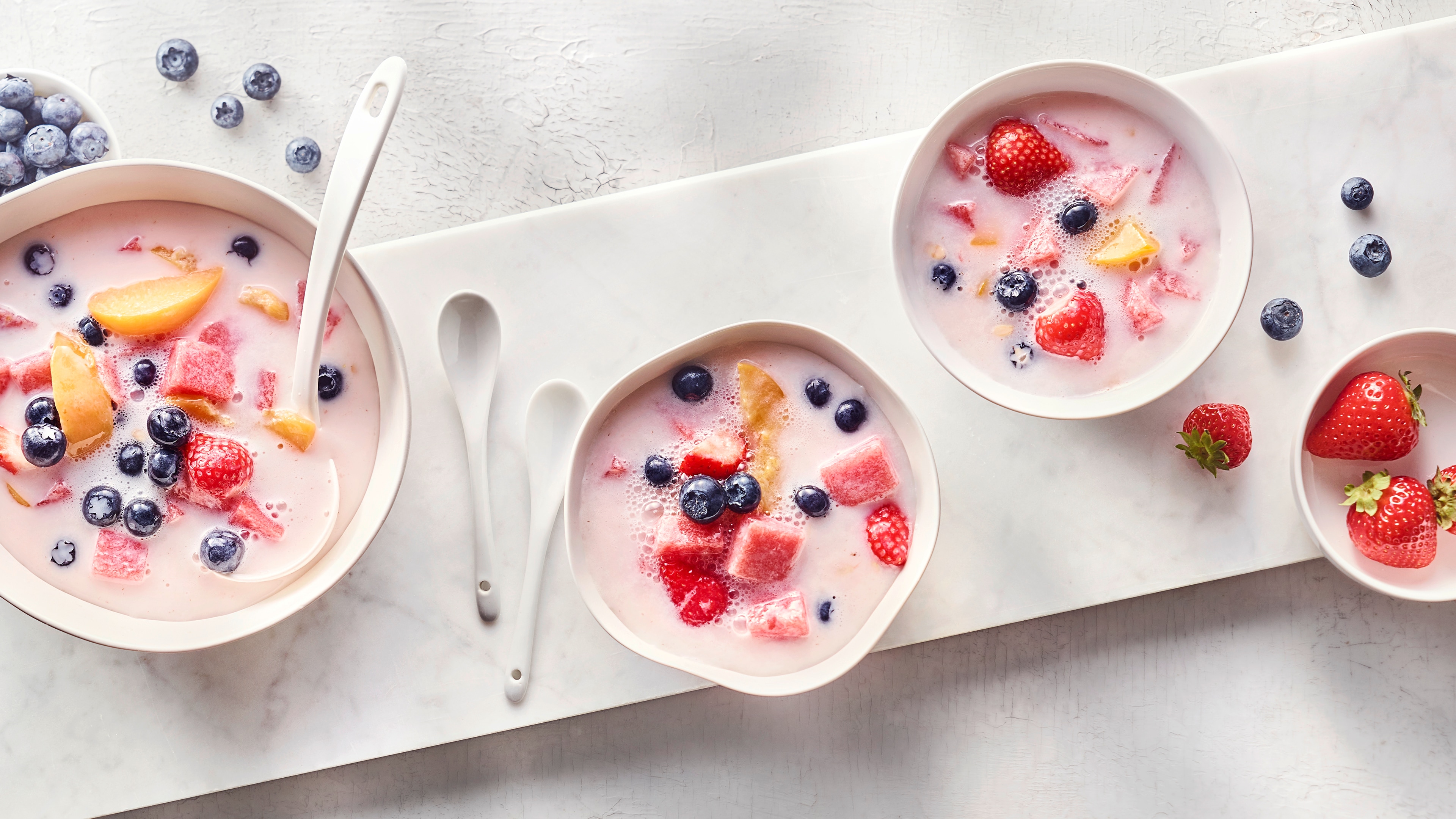Rezept für Hwachae Kleine Schälchen, gefüllt mit hellrosa, milchiger Fruchtpunsch mit frischen Erdbeeren, Blaubeeren, Pfirsich und Wassermelone.