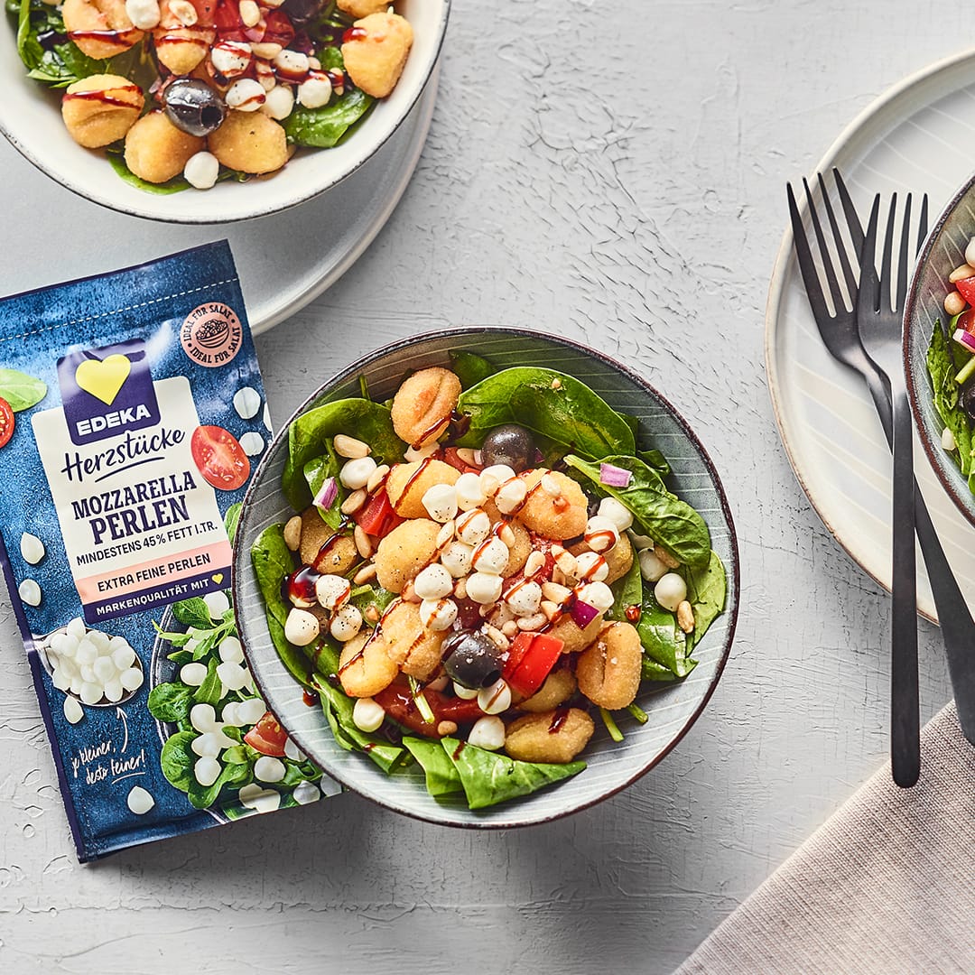 Salatbowl mit frischem Babyspinat, Gnocchi und Mozzarellaperlen in kleinen Schalen, daneben die EDEKA Herzstücke Mozzarella Perlen Packung.