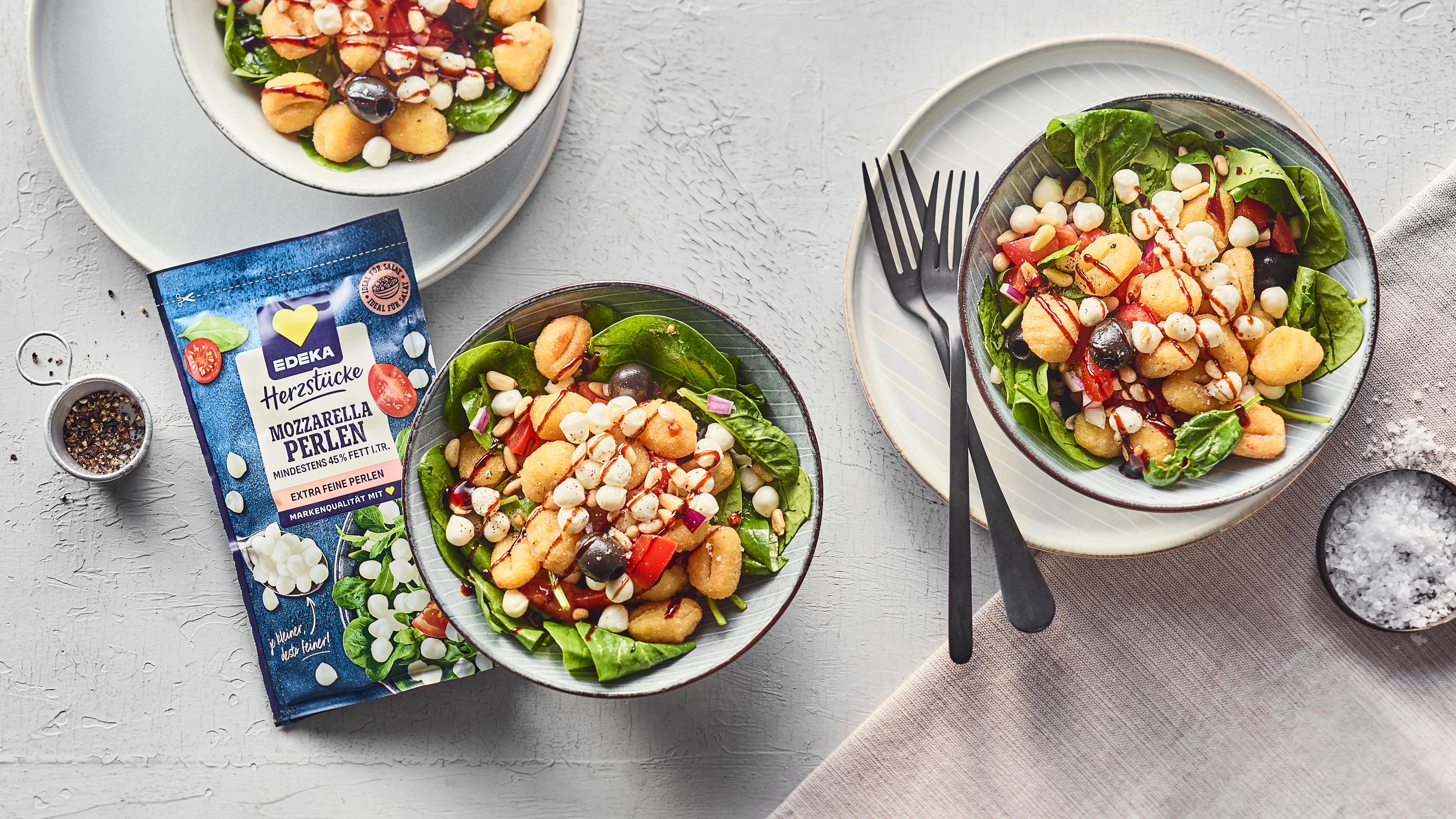 Rezept für Italian Bowl mit EDEKA Herzstücke Mozzarella Perlen Salatbowl mit frischem Babyspinat, Gnocchi und Mozzarellaperlen in kleinen Schalen, daneben die EDEKA Herzstücke Mozzarella Perlen Packung.
