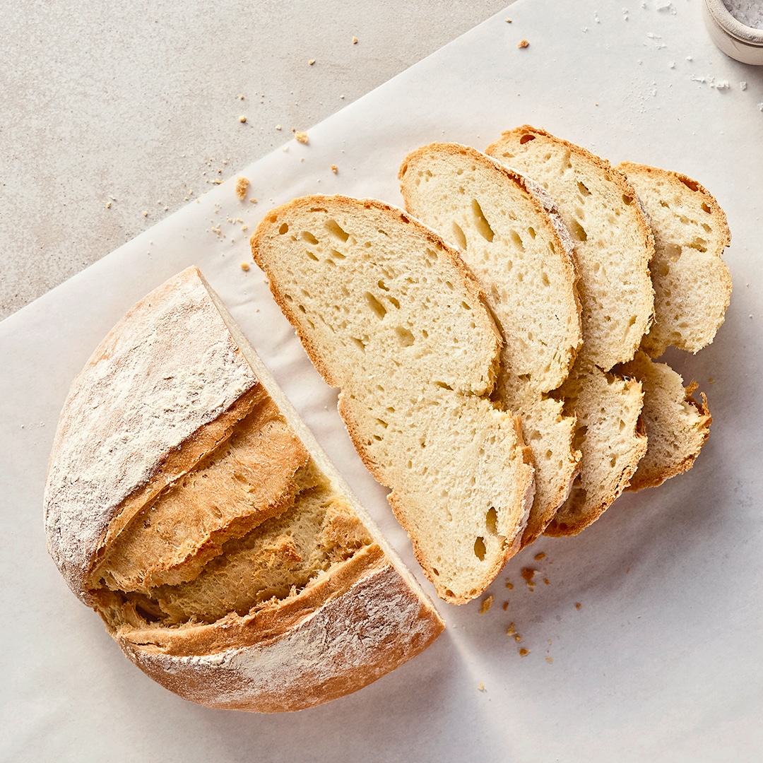 Ein Leib helles Brot mit einem fluffigen Teig und einer bemehlten, dicken, knusprigen Kruste, auf einem Stück Backpapier