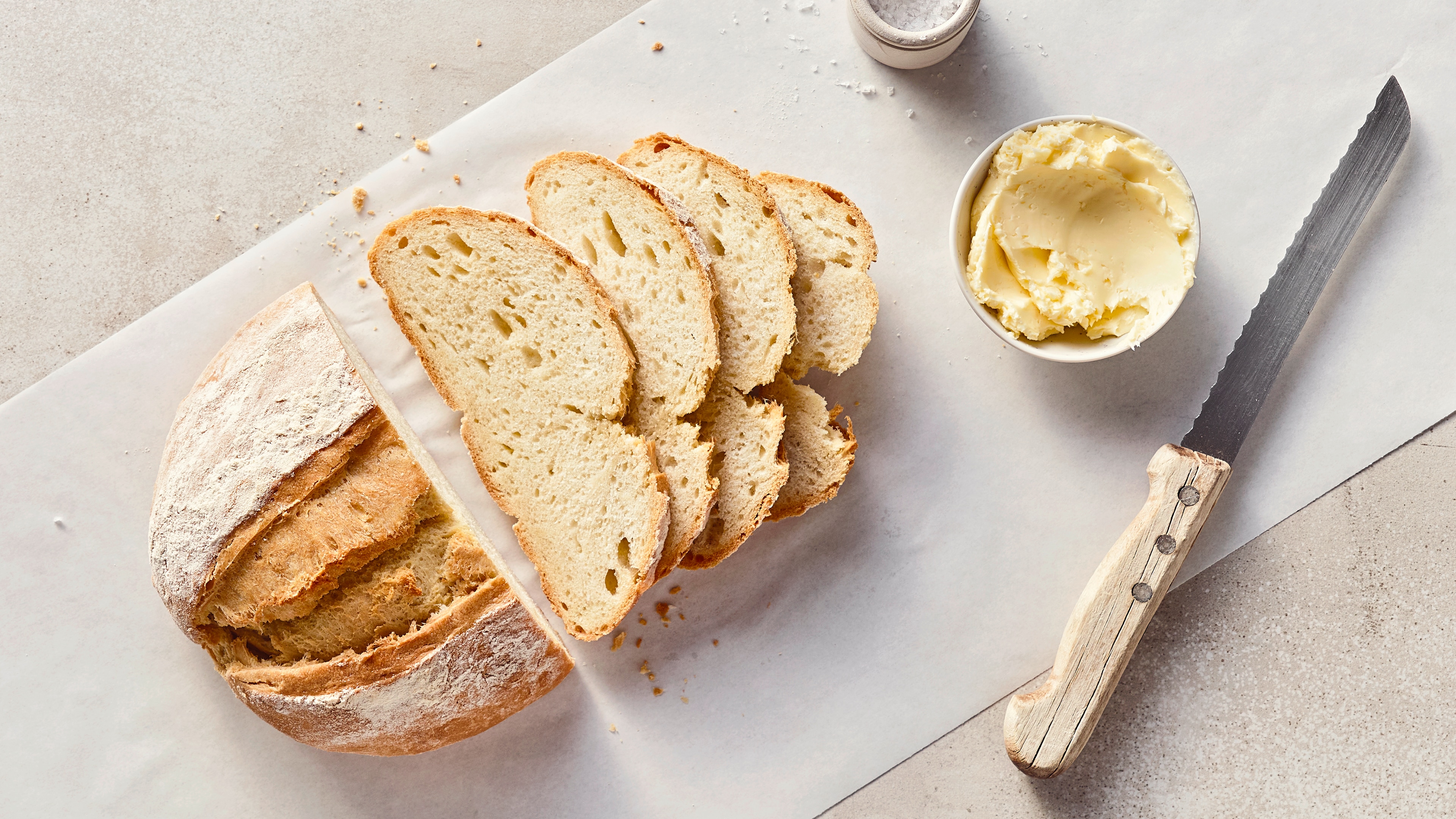 Ein Leib helles Brot mit einem fluffigen Teig und einer bemehlten, dicken, knusprigen Kruste, auf einem Stück Backpapier