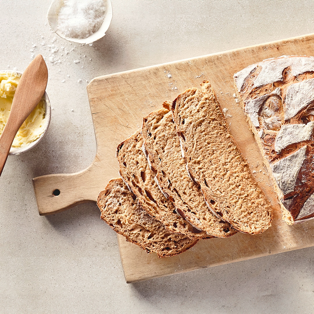 Ein Leib Brot mit einem saftigen Teig und einer knusprigen Kruste mit einem rautenförmigen Muster, auf einem Holzbrett