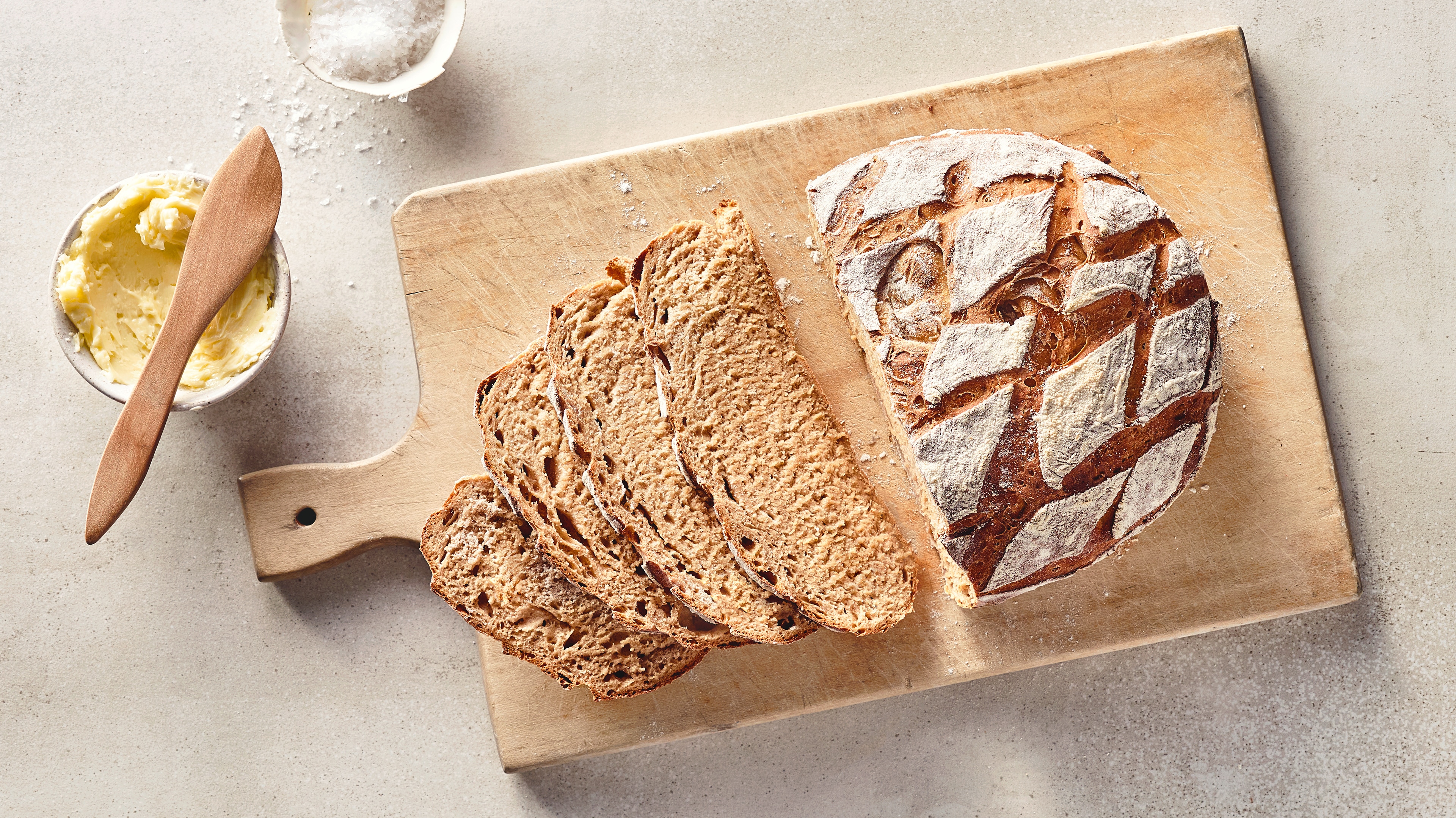 Ein Leib Brot mit einem saftigen Teig und einer knusprigen Kruste mit einem rautenförmigen Muster, auf einem Holzbrett