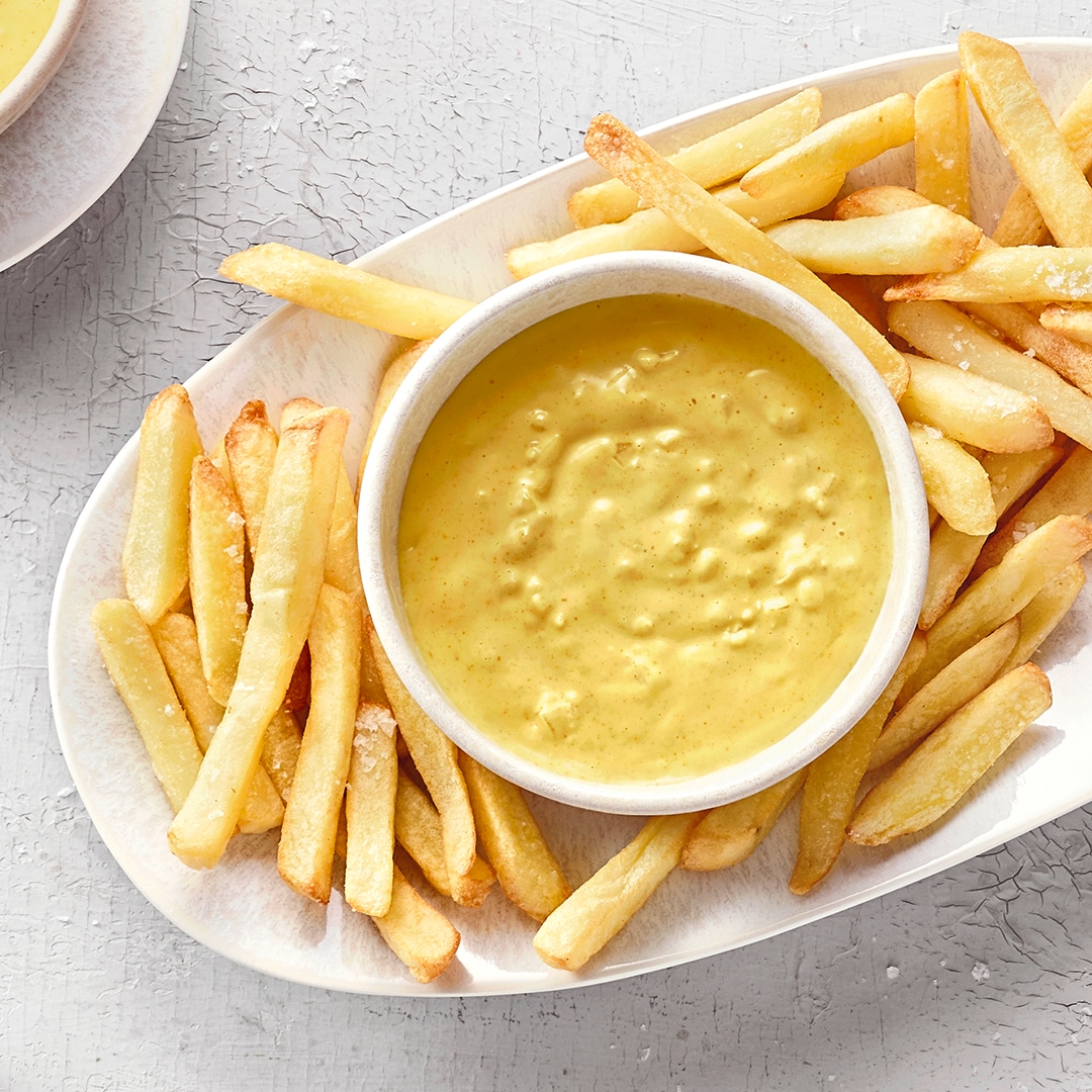 Großer ovaler Teller mit Pommes und einer kleinen Schale mit gelbem, cremigem, leicht stückigem Dip