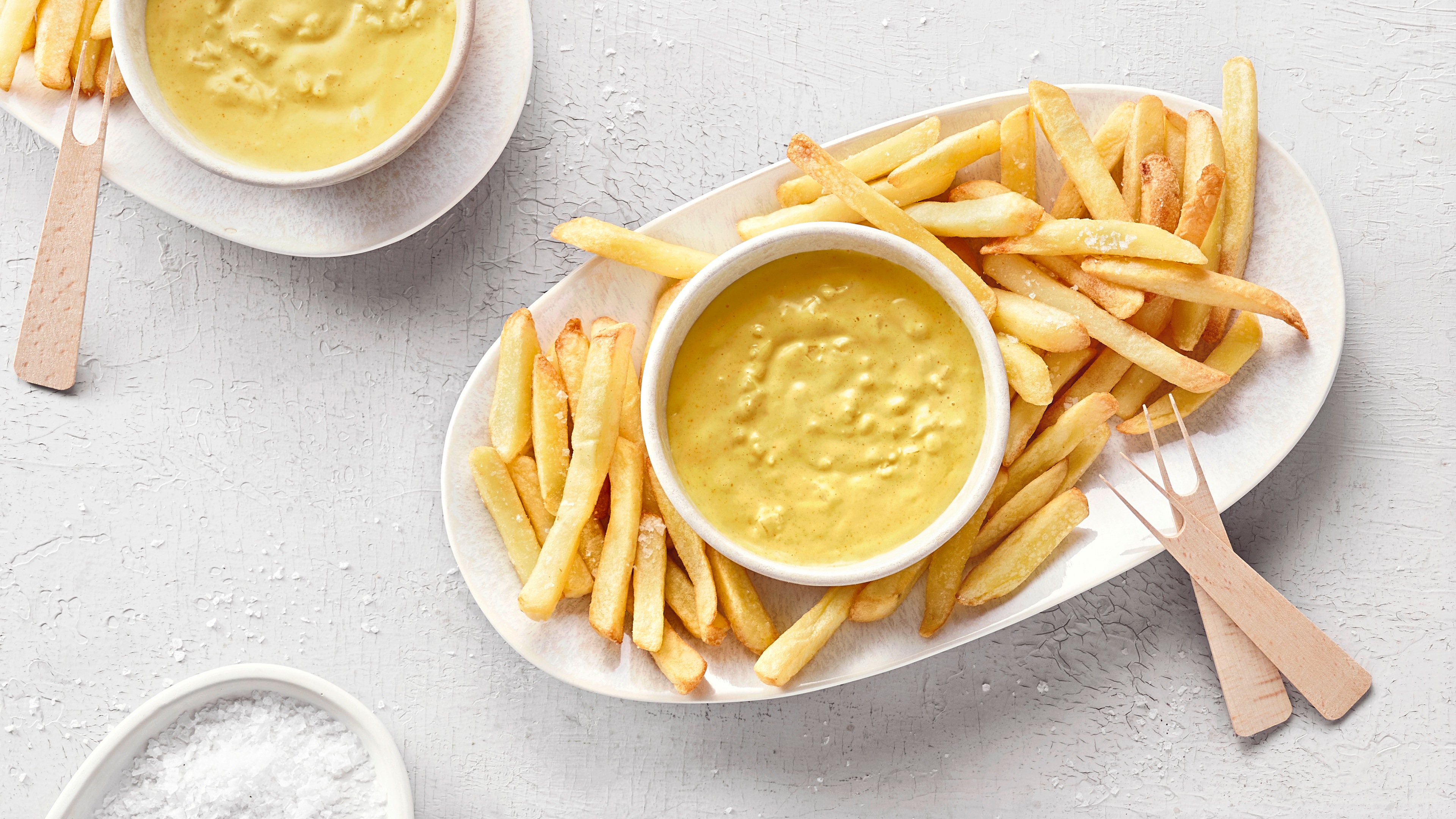 Großer ovaler Teller mit Pommes und einer kleinen Schale mit gelbem, cremigem, leicht stückigem Dip