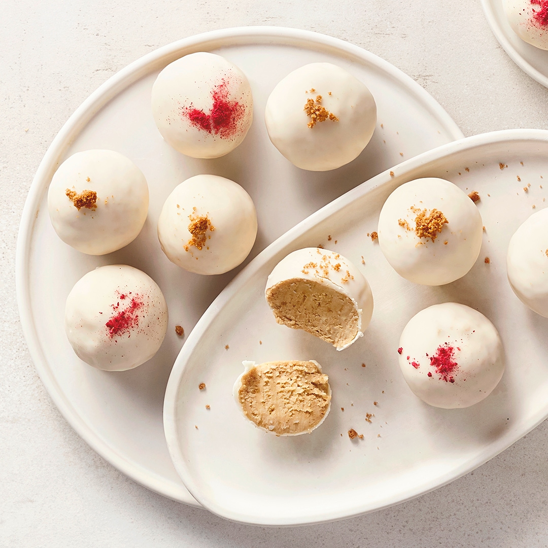 Ein Teller mit weißen Kugeln, mit rotem Pulver oder braunen Krümeln bestreut, sowie einer angeschnittenen Kugel.