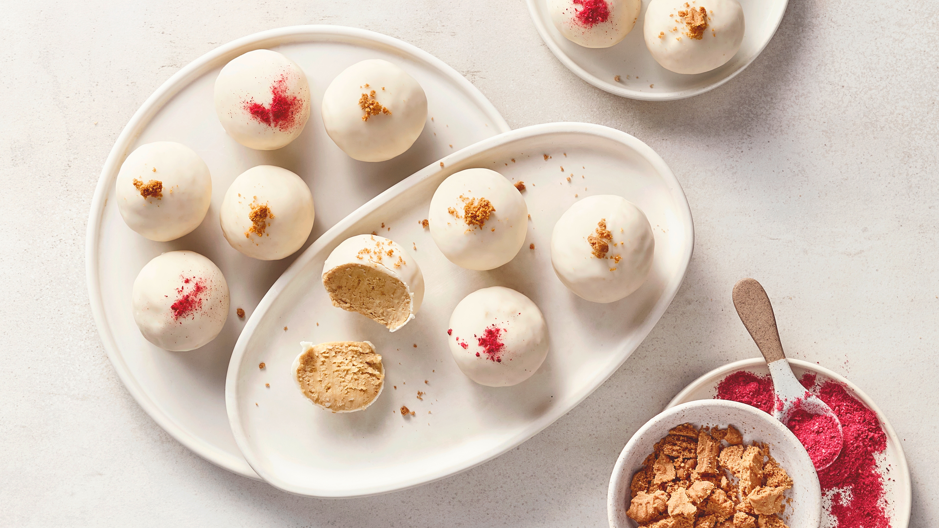Ein Teller mit weißen Kugeln, mit rotem Pulver oder braunen Krümeln bestreut, sowie einer angeschnittenen Kugel.