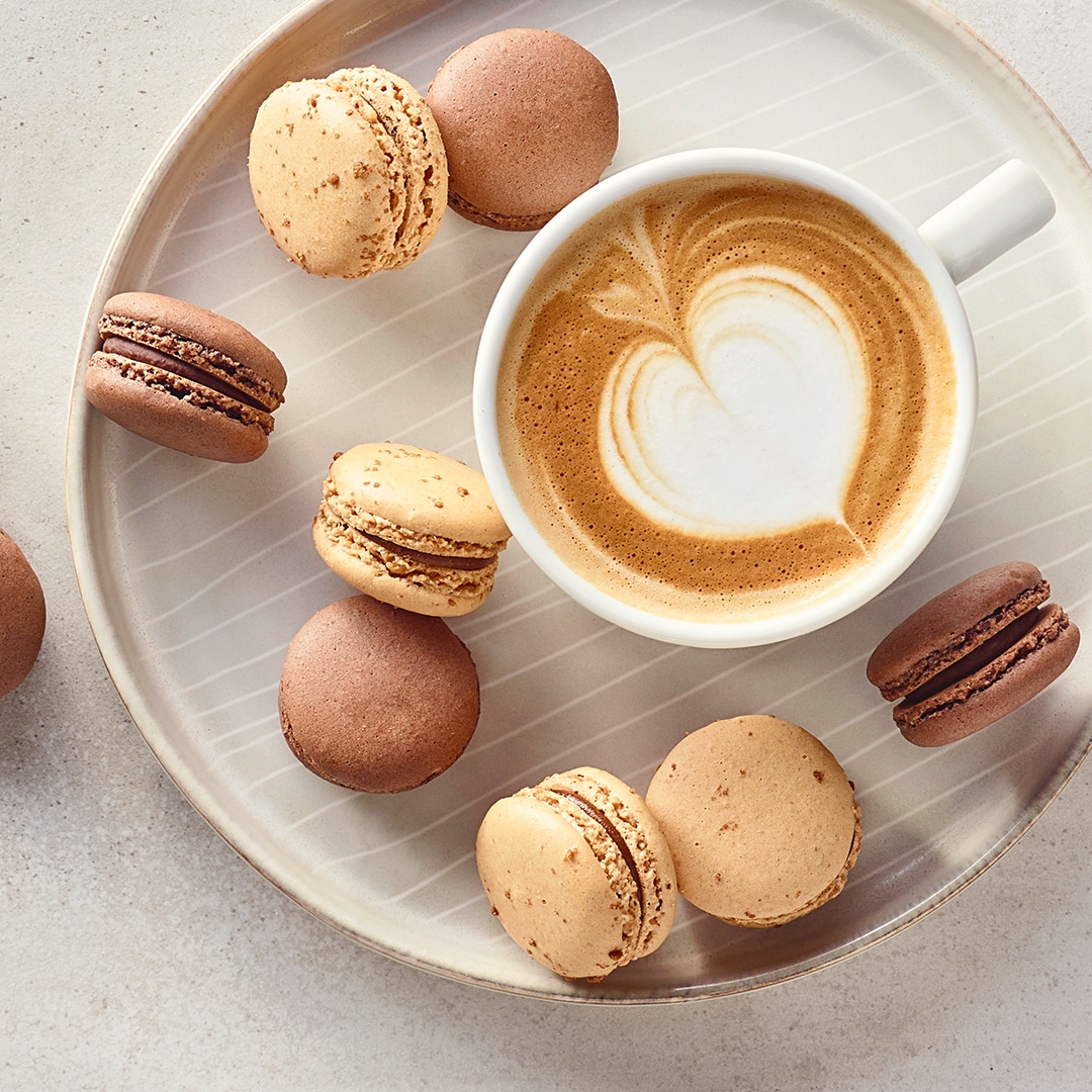 Ein Teller mit braunen und beigen Macarons und einer Tasse Kaffee