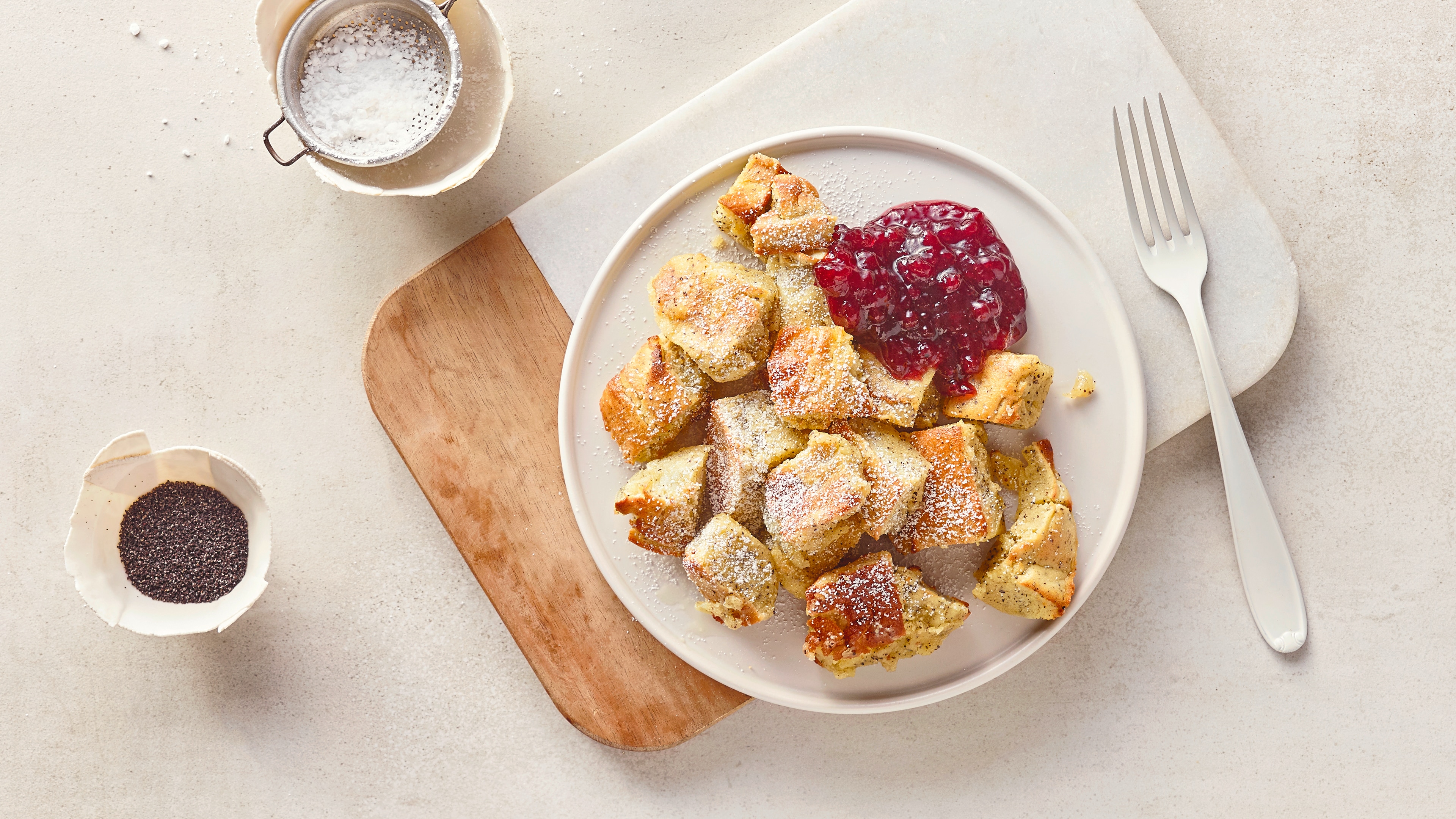 Rezept für Kaiserschmarrn aus dem Airfryer Ein Teller mit fluffigen, hellen Teigstücken, gemischt mit Mohn, bestreut mit Puderzucker, daneben ein Klecks Preiselbeeren