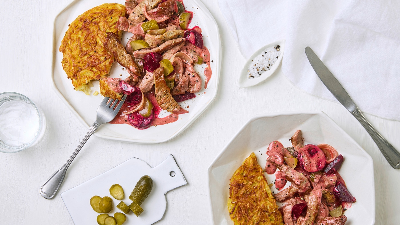 Teller mit Kartoffel-Rösti, gebratenen Fleischstückchen, Gewürzgurken und Rote Bete, in roter Soße