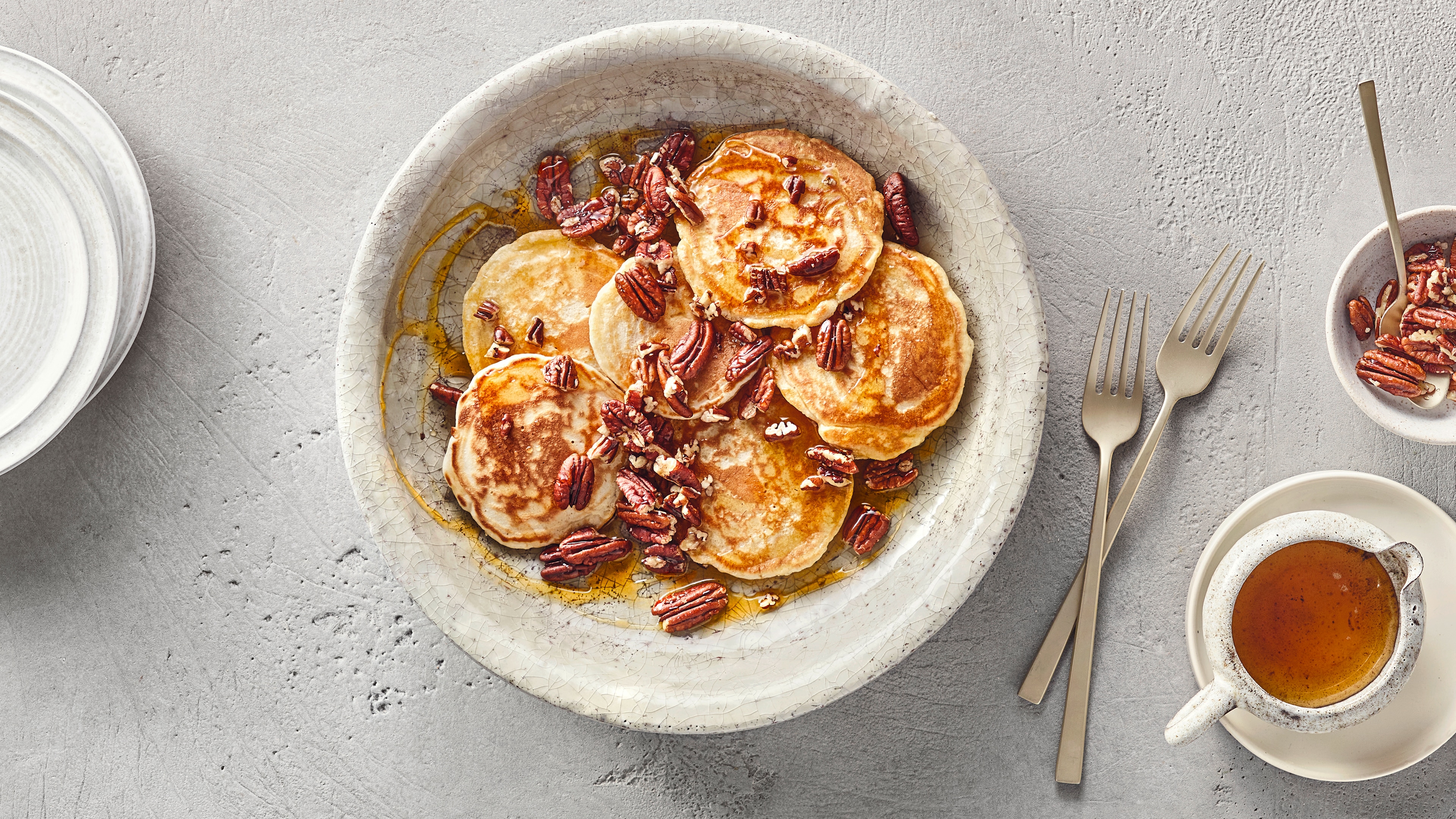 Ein Teller mit kleinen runden Pfannkuchen, braunen Pekannüssen und goldener Flüssigkeit.