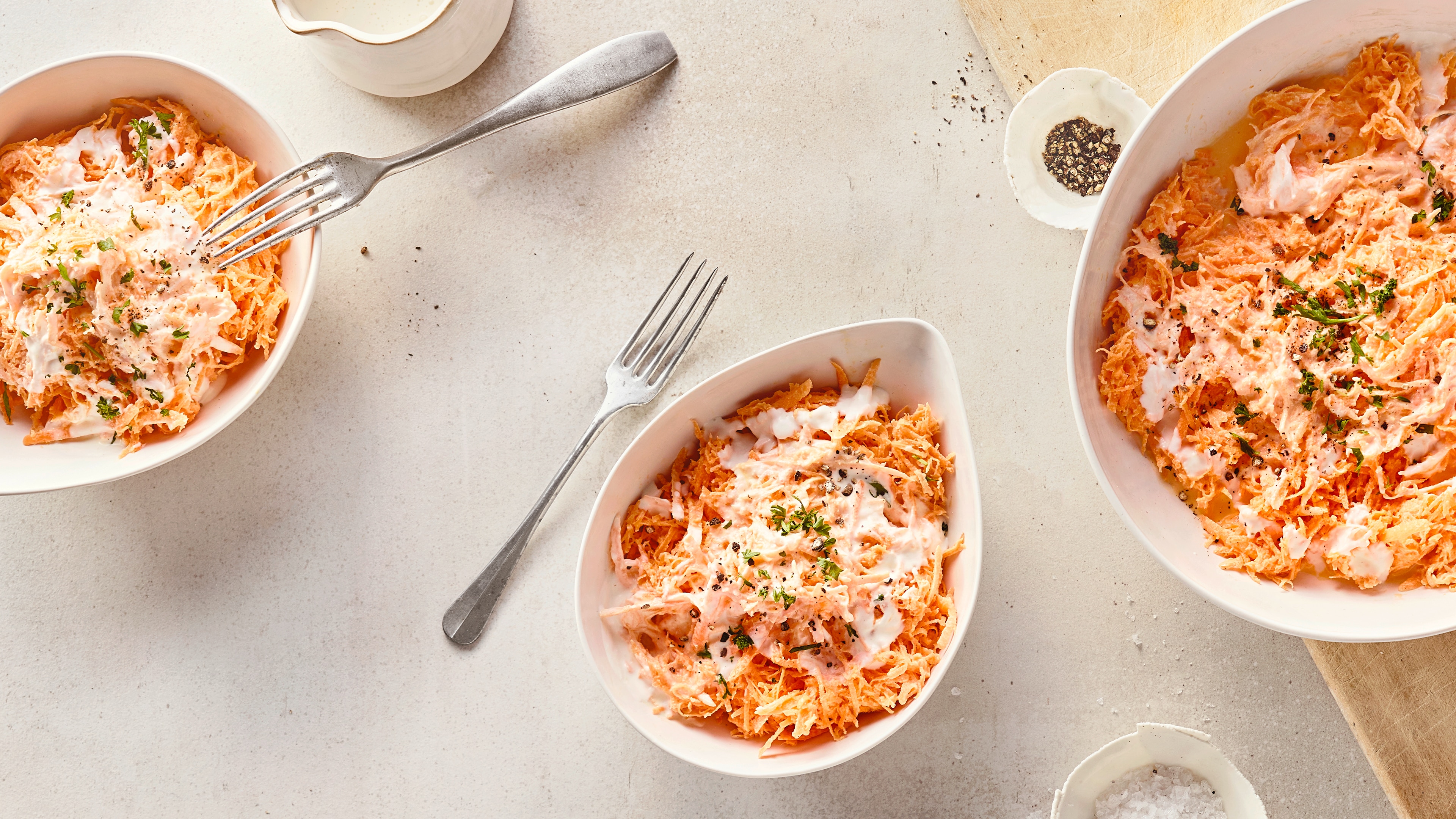 Rezept für Karottensalat mit Sahne Tropfenförmige Keramikschalen mit geraspelten Möhren und einer hellen Soße, getoppt mit gehackten Kräutern