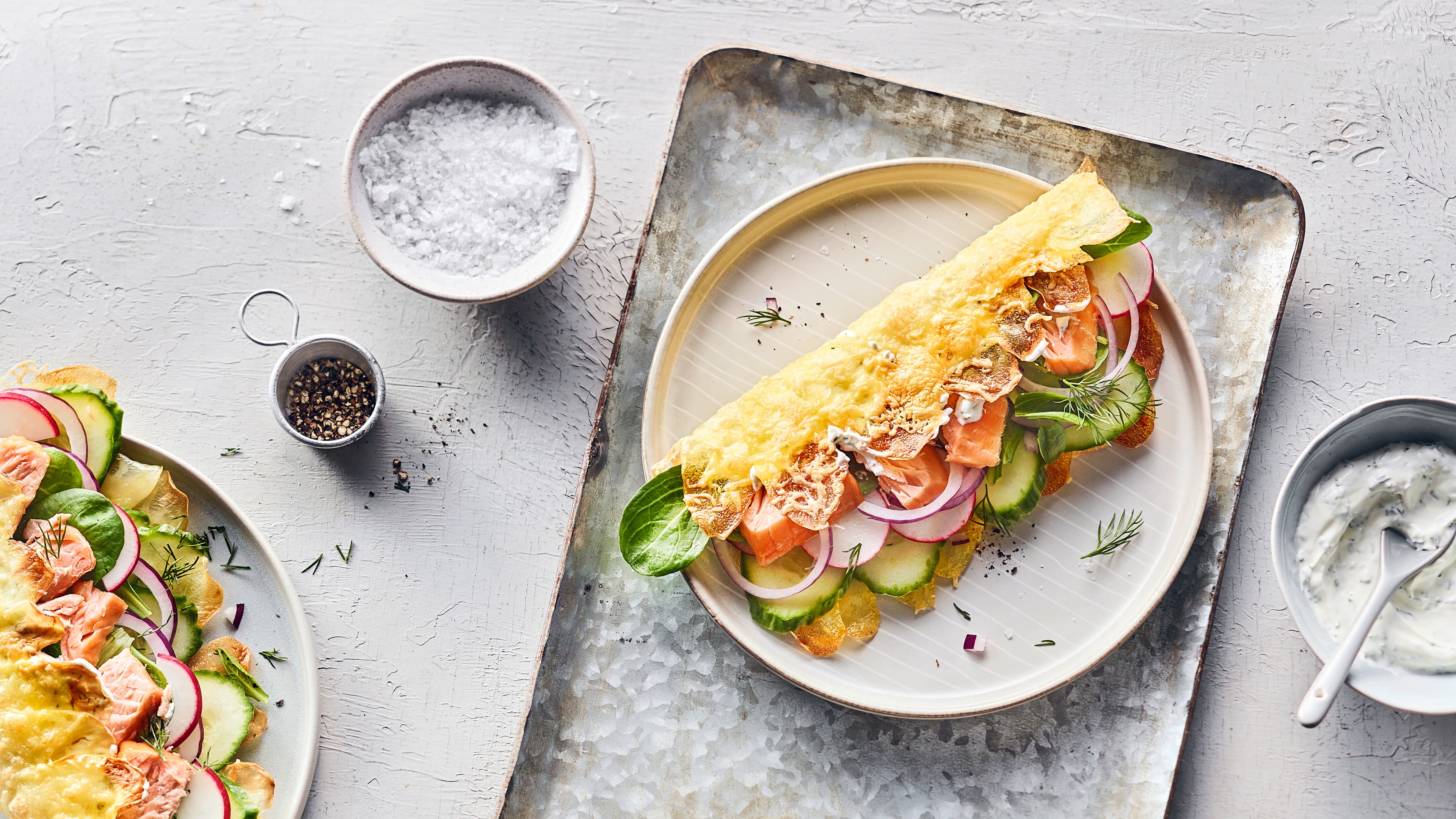 Rezepft für ein Kartoffel-Sandwich mit Stremellachs Ein Klappsandwich mit einer knusprigen Kartoffelkäsekruste, Gemüse und Stremellachsstücken auf einem runden Teller.